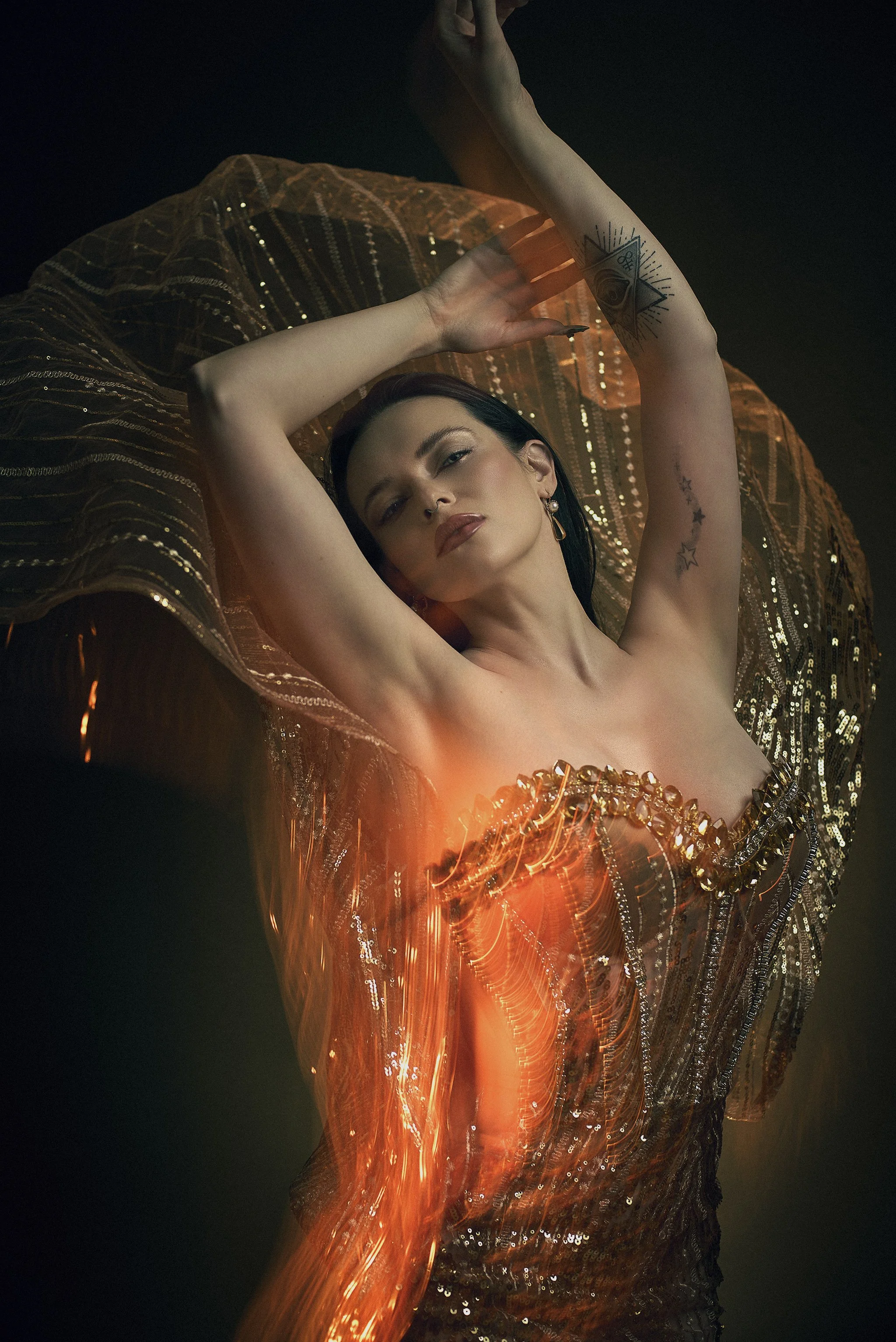 Luxury boudoir photography in golden tones featuring a woman posing with raised arms, motion blur, shimmering fabric and cinematic lighting.