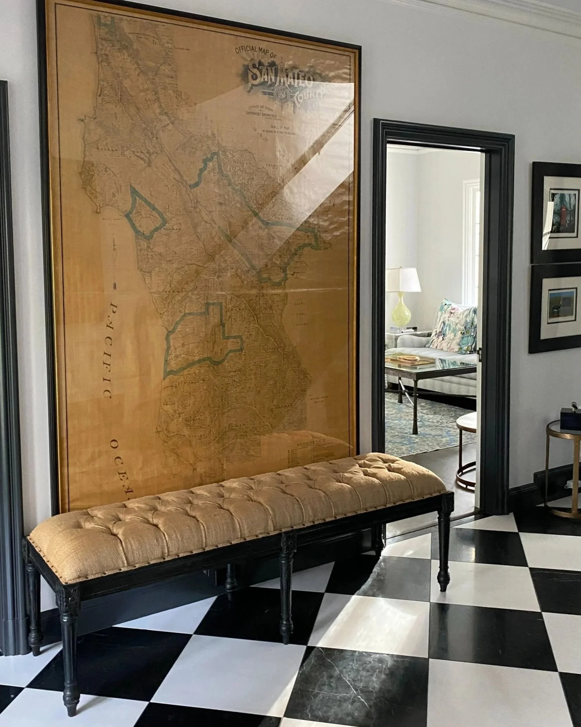 Interior entryway with black and white marble flooring. A burlap upholstered bench with an original framed cadastral map of San Mateo on the wall behind.