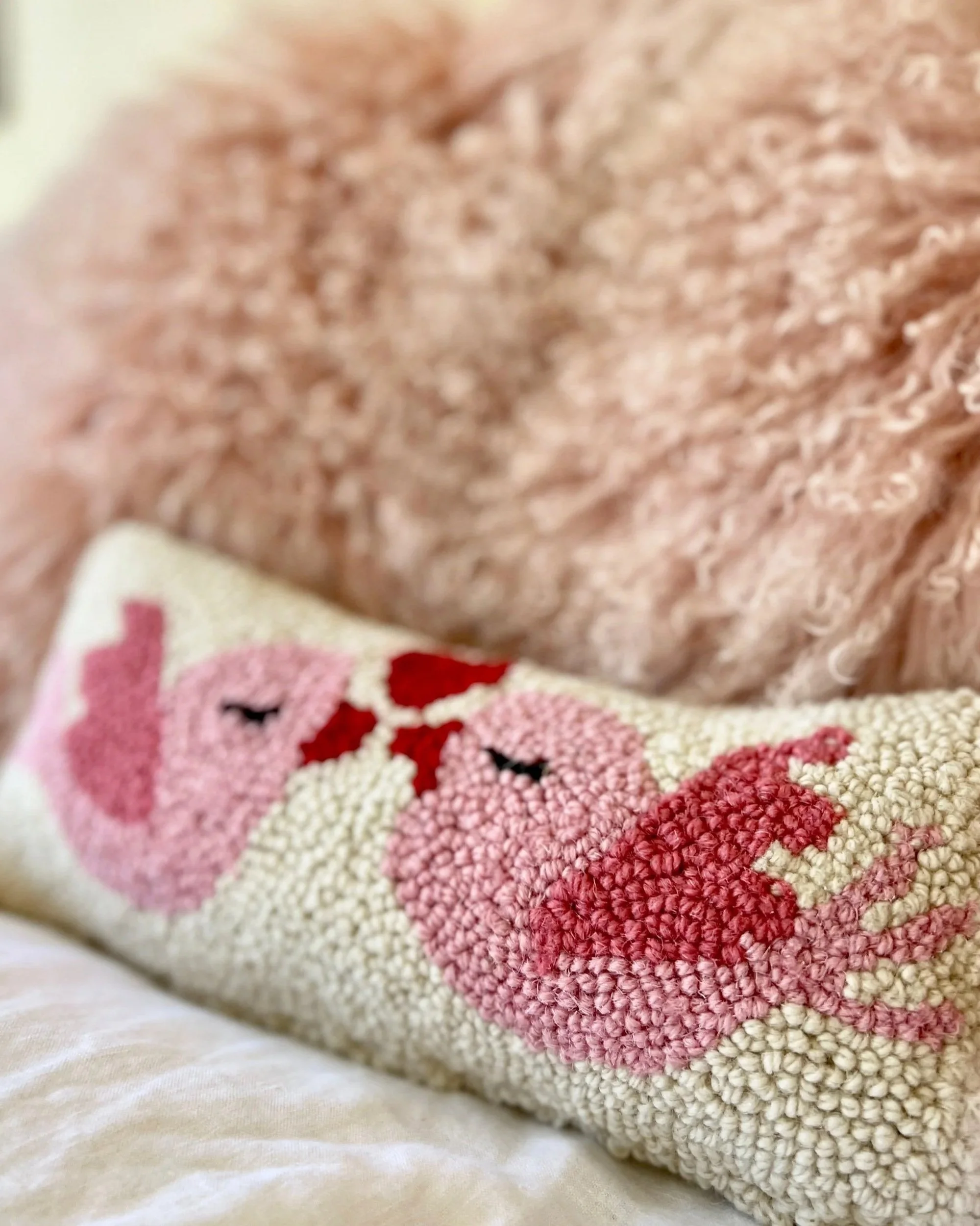 Pink shearling throw pillows, with a needlepoint accent pillow, decorated with two pink kissing lovebirds.