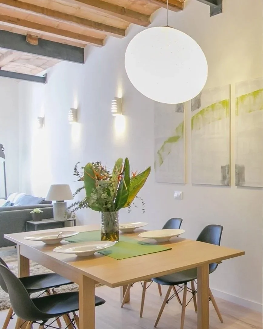 Dining table in a Barcelona apartment. Catalan ceilings with Moooi light above a wooden table with four chairs. Set for dinner with white bowls and tropical flowers.