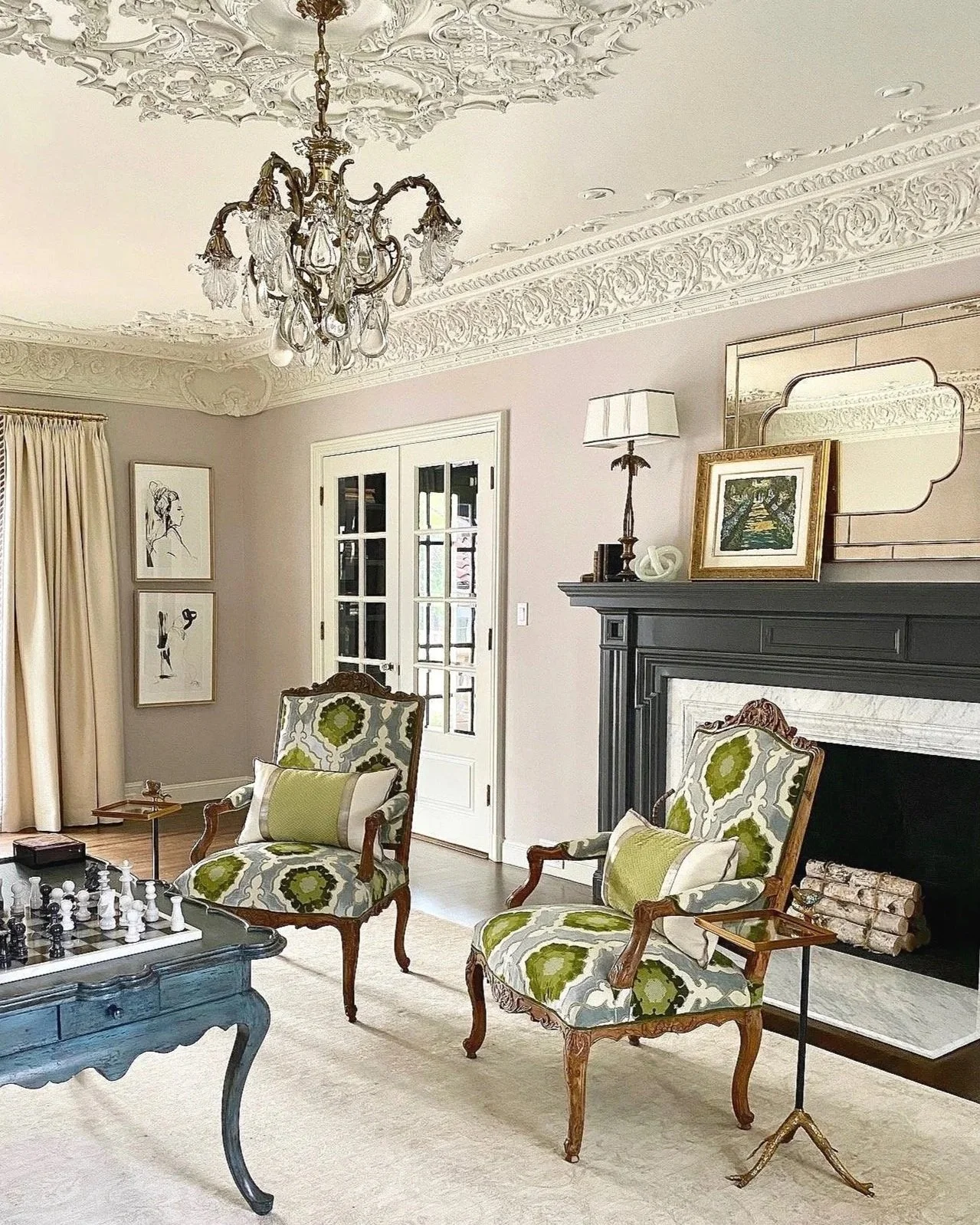 Formal living room with ornate custom plaster ceiling, and Belle Epoch vintage crystal chandelier. Two 17th century french chairs, upholstered in silk  velvet damask. in front of a fireplace mantle.