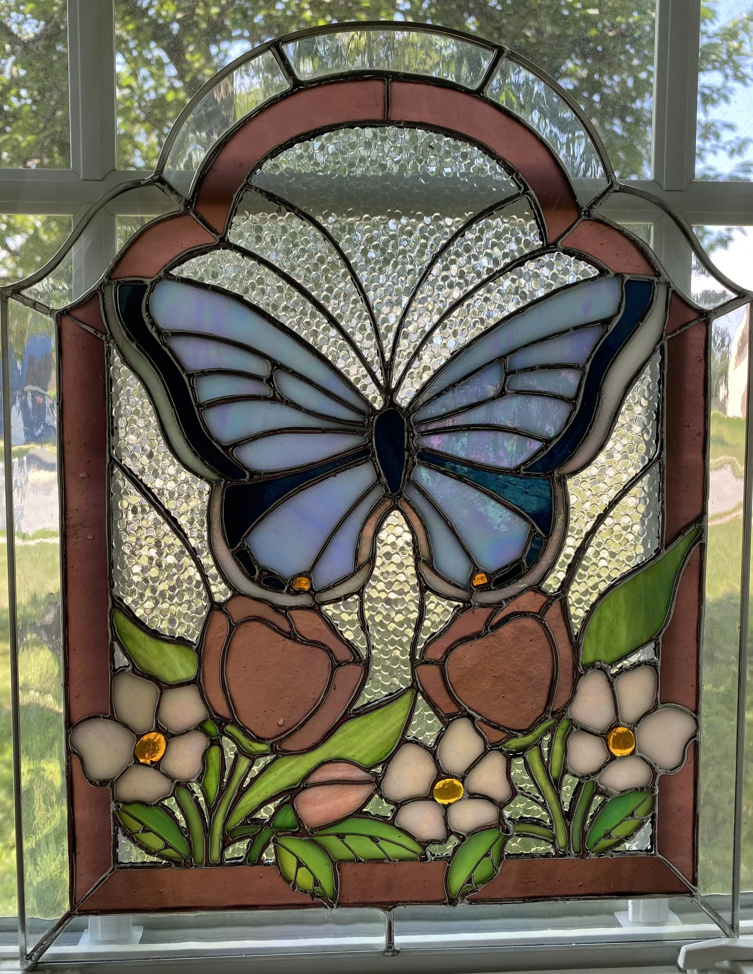 A stained glass panel with a butterfly over flowers