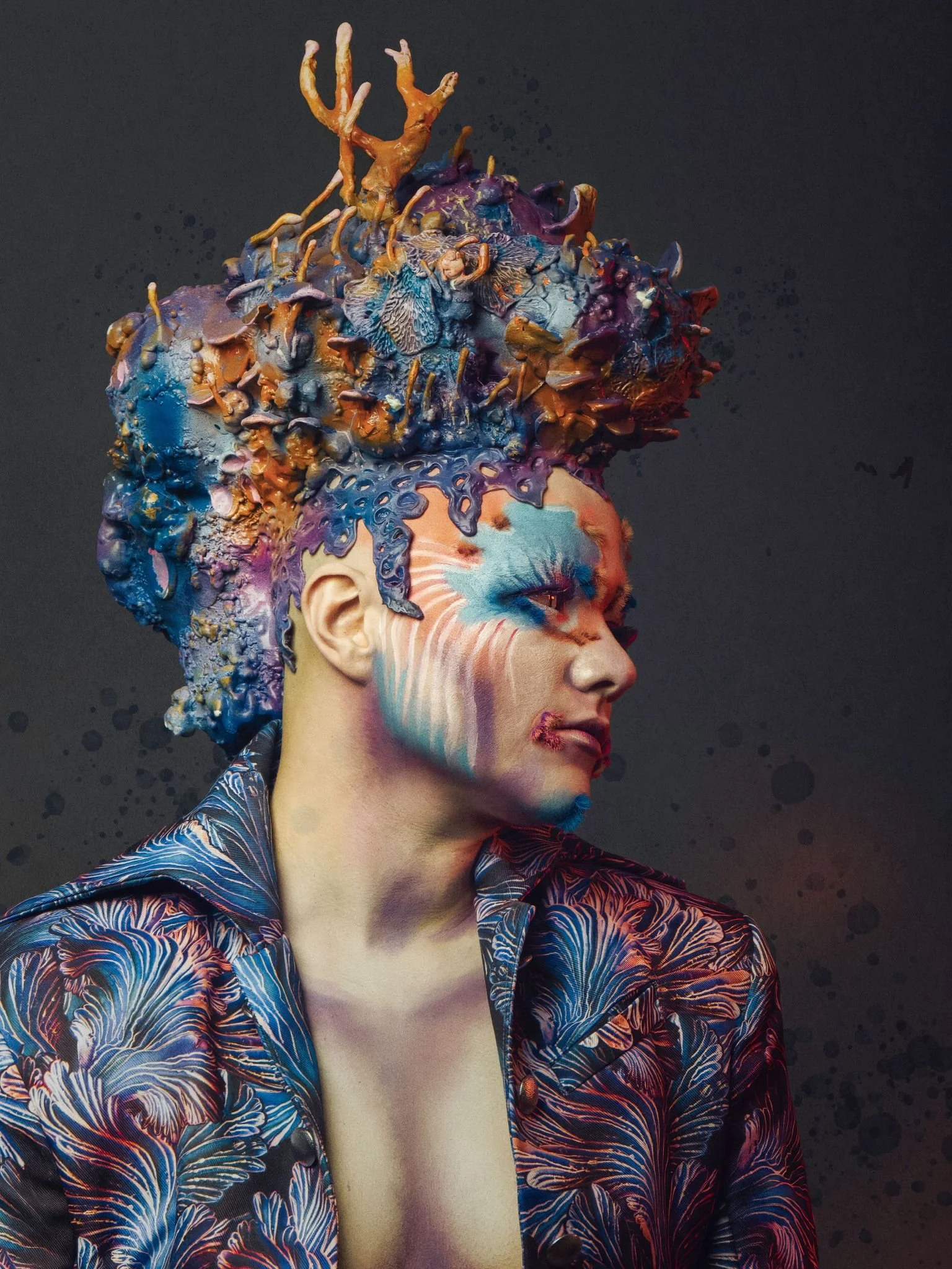 A person in drag with a mushroom sculpture headpiece, dressed in a custom mushroom jacket by Shhhroooms wearing beautiful makeup.
