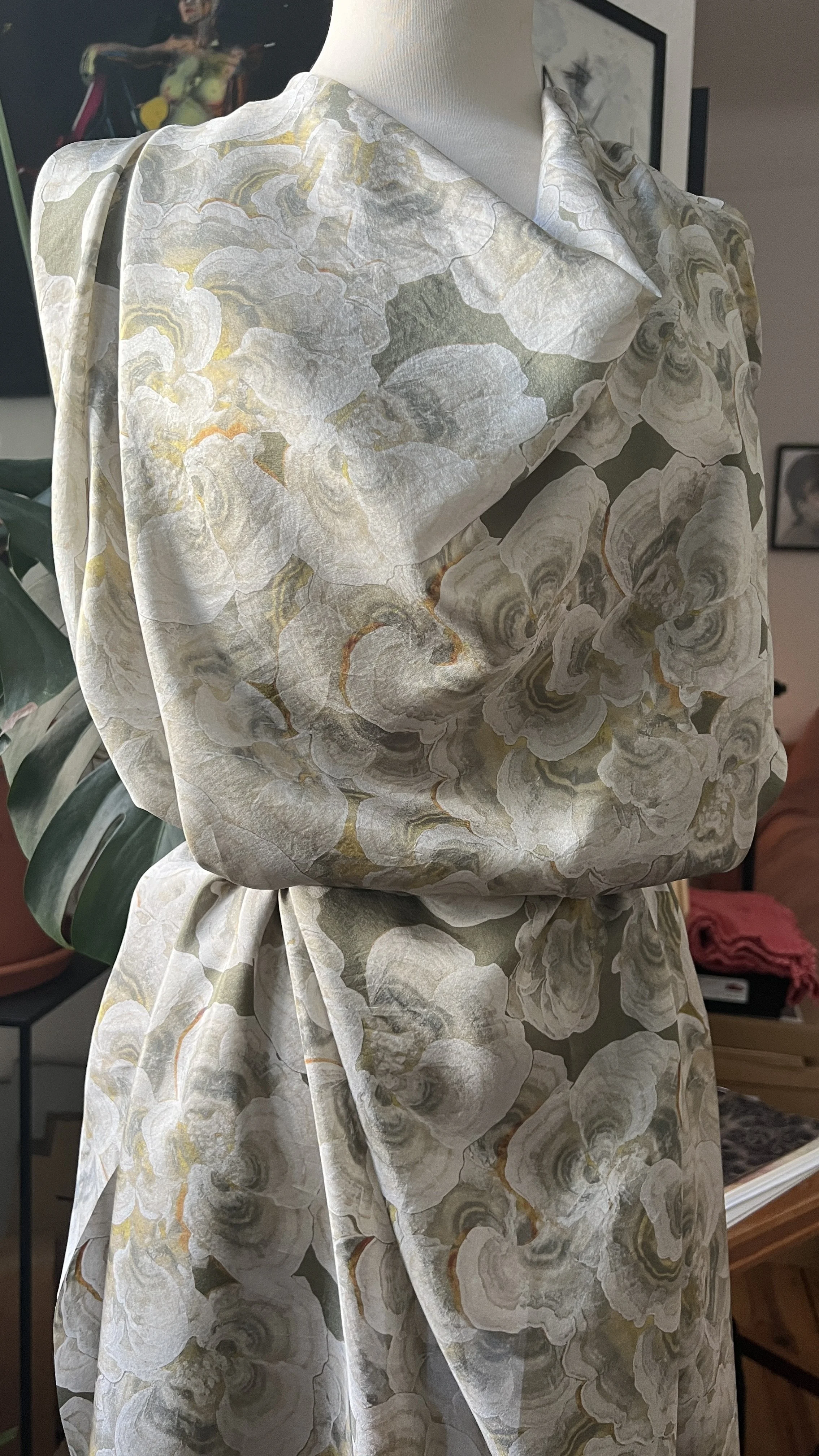 Close-up of a mannequin wearing a floral-like pattern that is actually turkey tail mushrooms. Fabric is silk, draped, soft-colored flowery mushroom shapes in shades of white, gray, and light yellow, with some hints of orange.