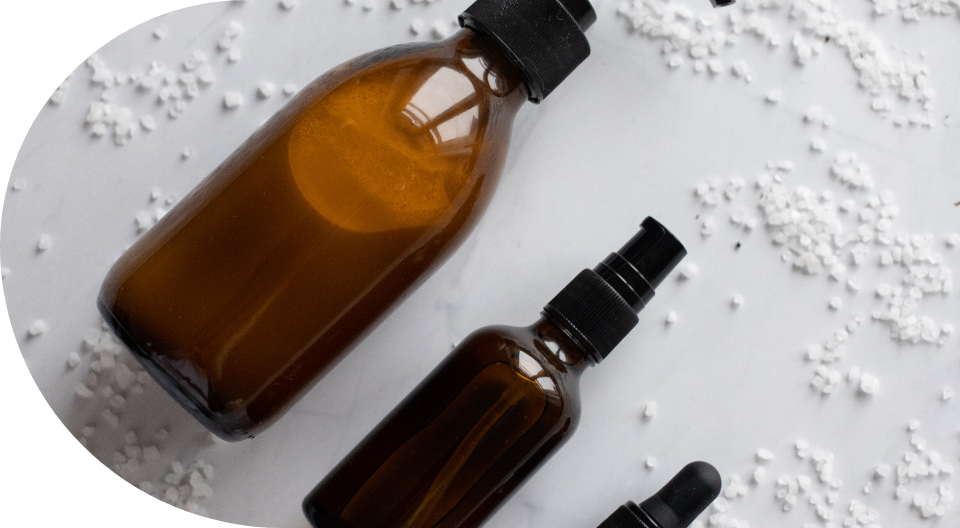 Brown glass bottles with black caps surrounded by small white granules on a white surface.