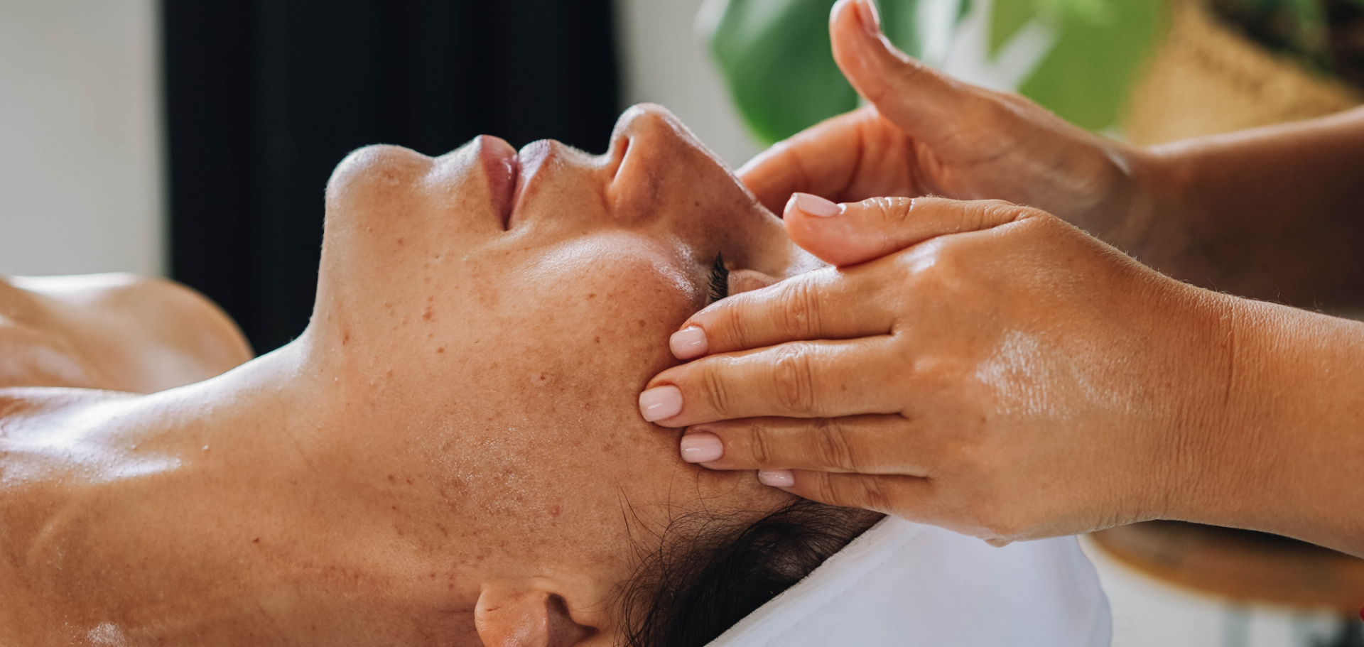 Person receiving a facial massage with visible hands applying cream on the forehead