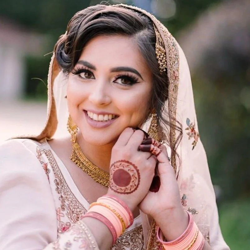 Smiling bride in traditional attire with henna designs on her hand and colorful bangles.