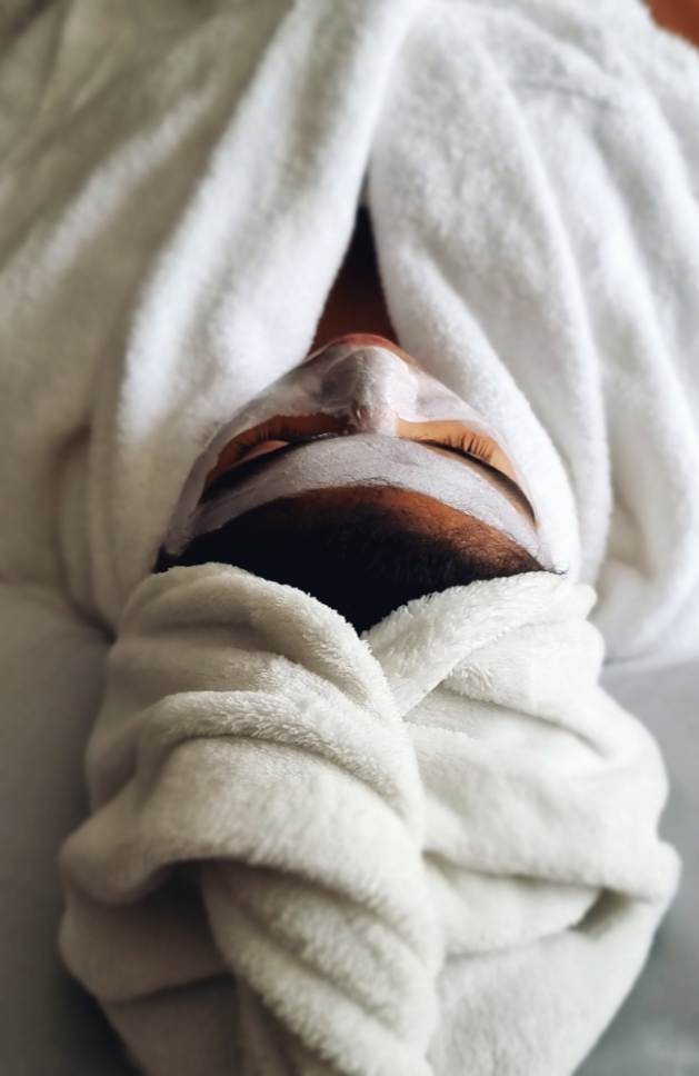 Person with a white facial mask covered in a white towel at a spa.