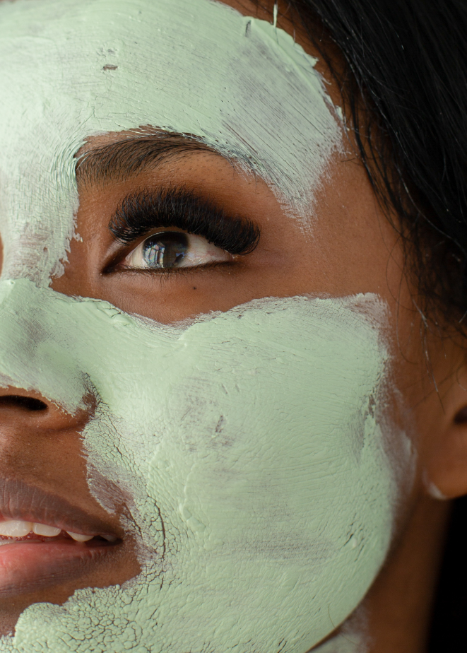 Close-up of a person's face with a green facial mask applied, focusing on their eye and lips slightly visible.