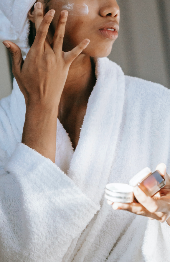 Person applying face cream while wearing a bathrobe and head towel.