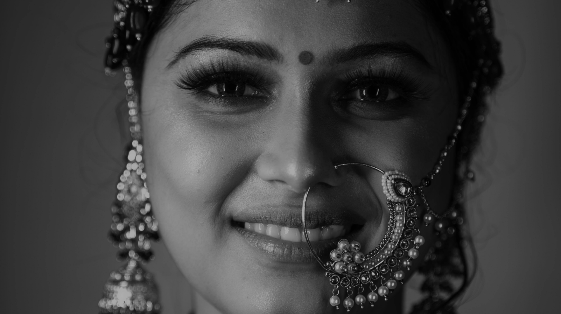 Close-up portrait of a woman smiling, wearing traditional jewelry including a decorative nose ring and earrings.