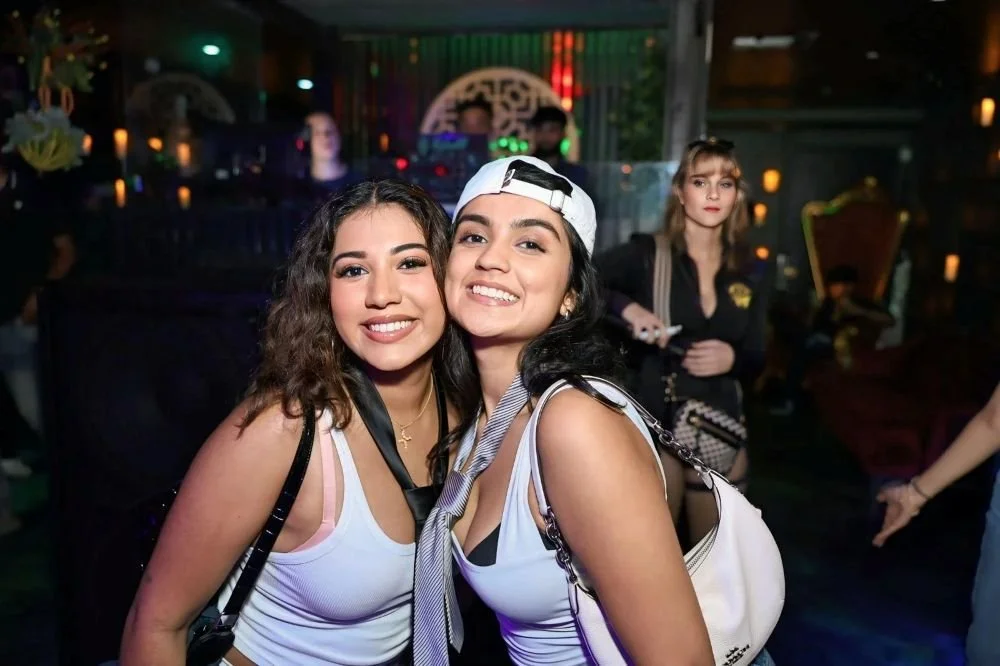 Two women in white shirts posing at a nightclub