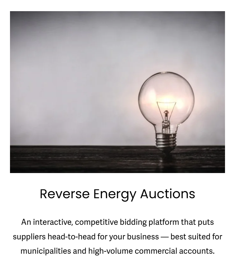 A clear incandescent light bulb sitting on a dark wooden surface with a plain, light gray background.