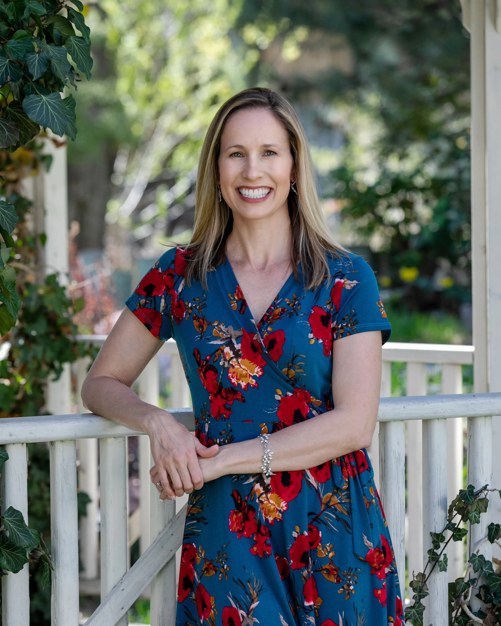 Woman in a black dress standing in a bright room with large angled windows and white wooden floor.