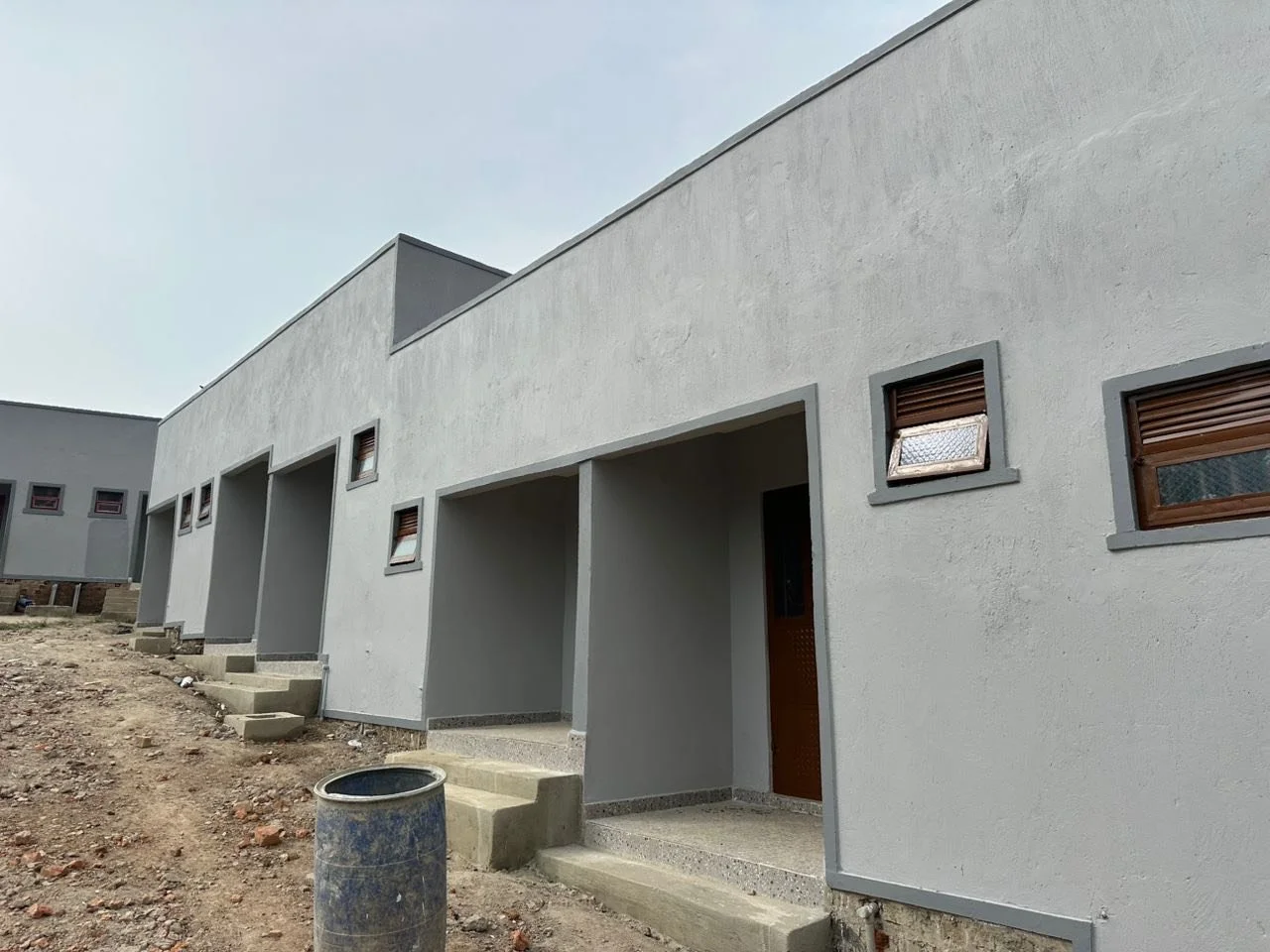 Newly constructed white modern townhouses with small windows, steps leading to entrances, and a construction barrel in the foreground.