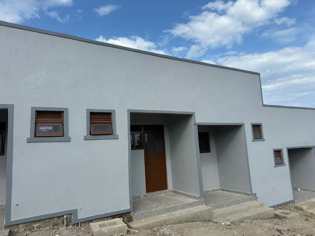 Modern white residential building with multiple small windows and concrete steps at the entrance, under a partly cloudy sky.