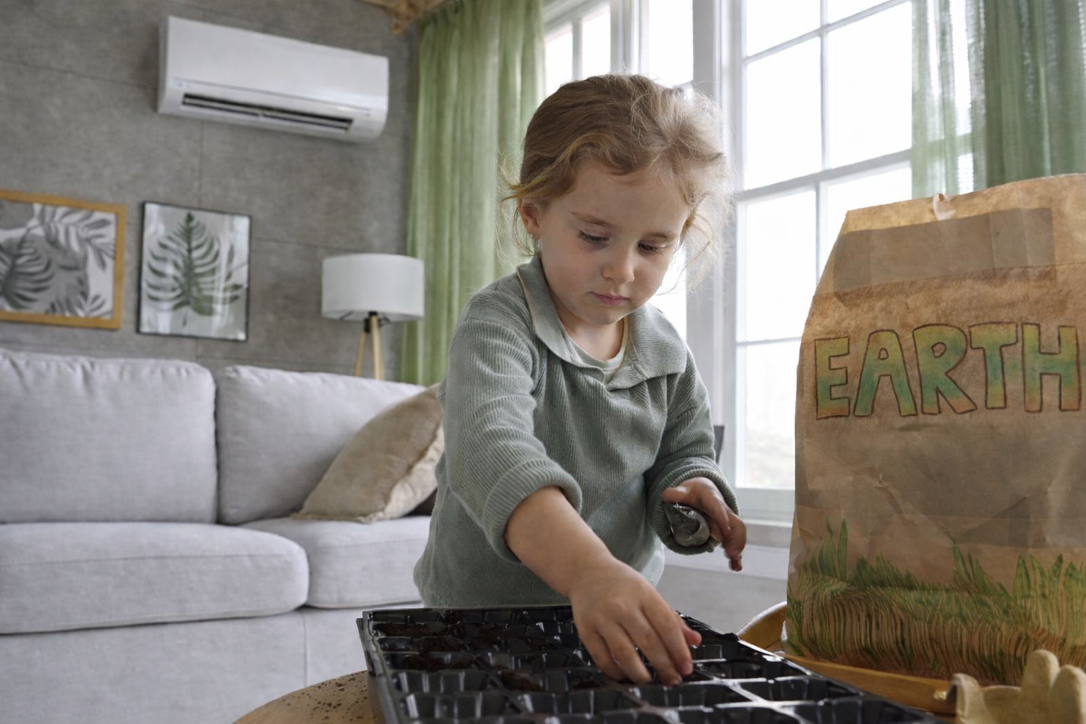 Child planting seeds indoors with mini-split heat pump and ‘EARTH’ bag.