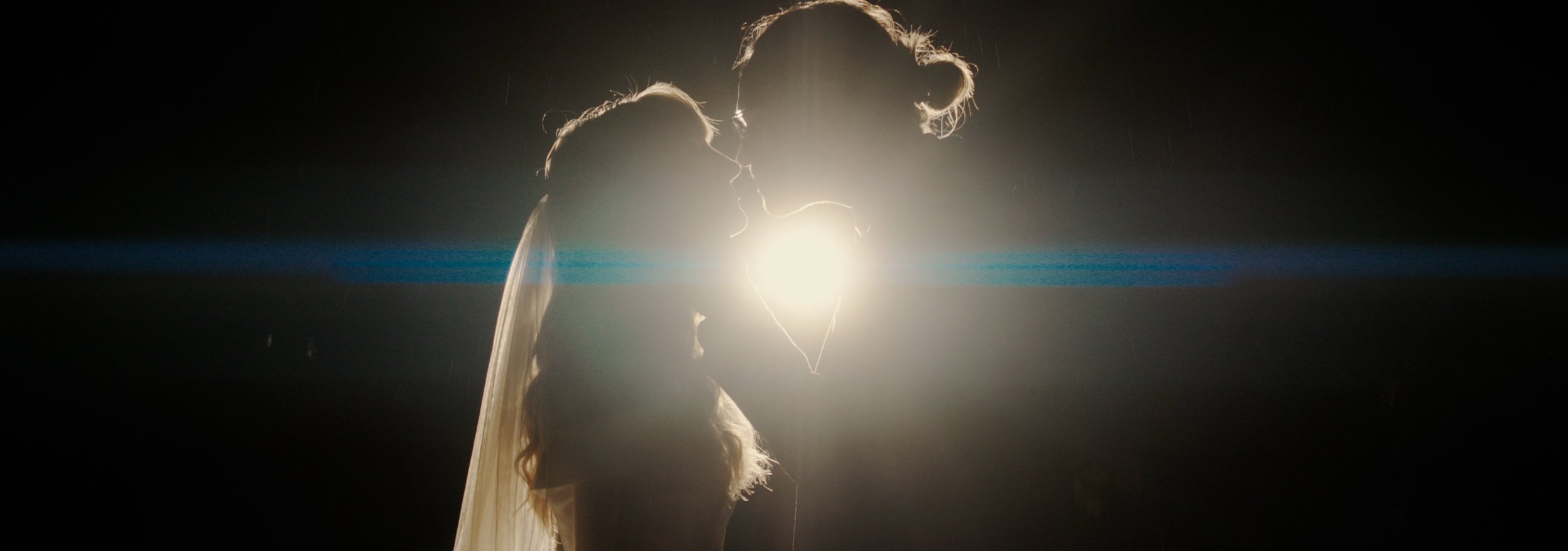 Silhouettes of a couple about to kiss, backlit by a bright light, creating a dramatic effect.