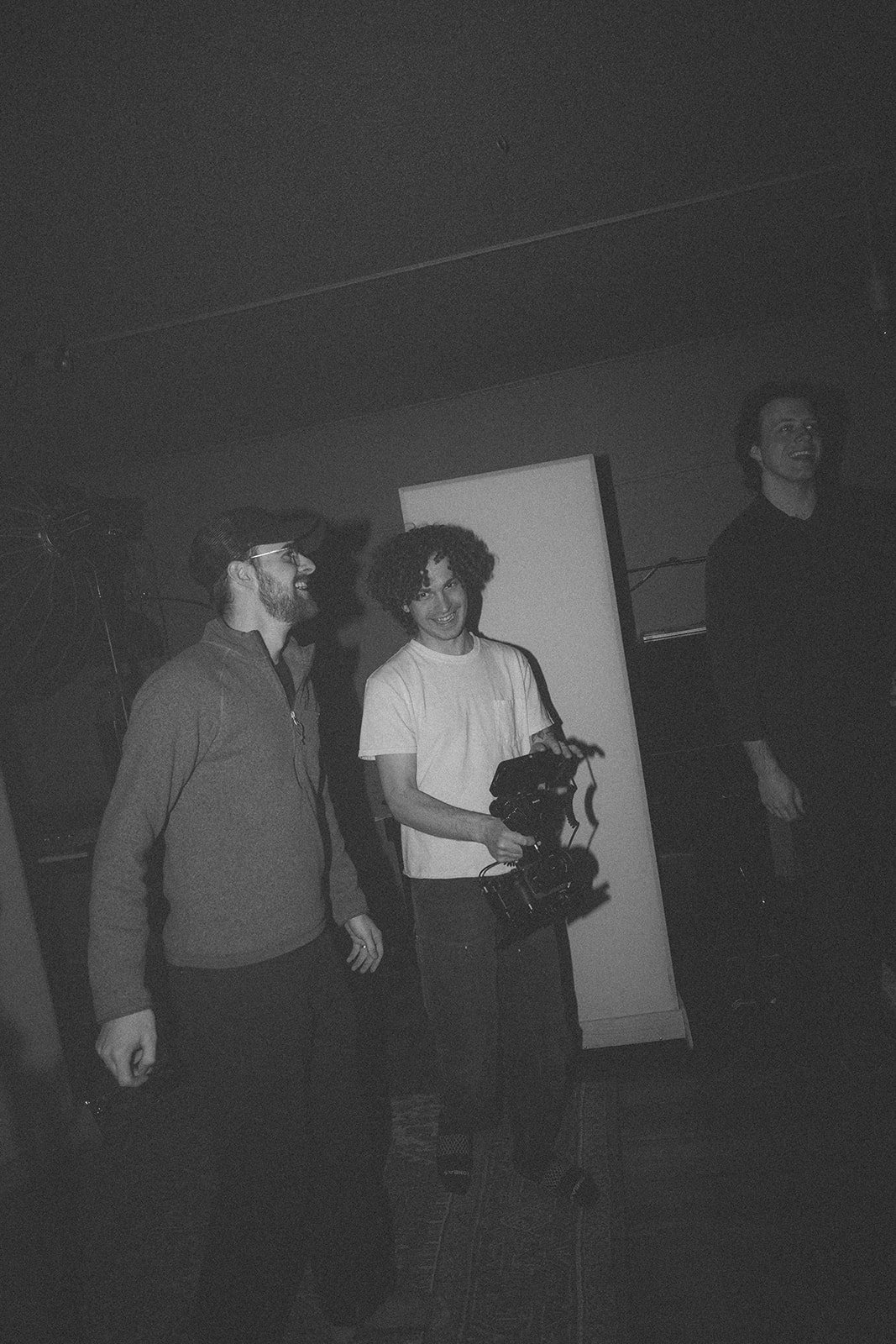 Three people indoors, one holding a camera, in a dimly lit setting.