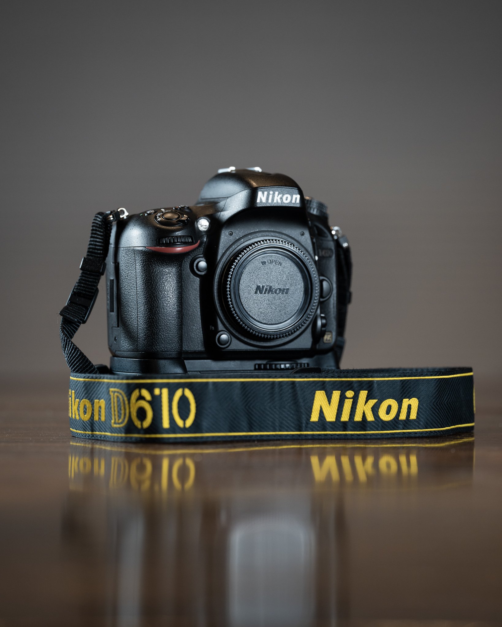 Nikon D610 camera with a black strap, displayed on a reflective surface.