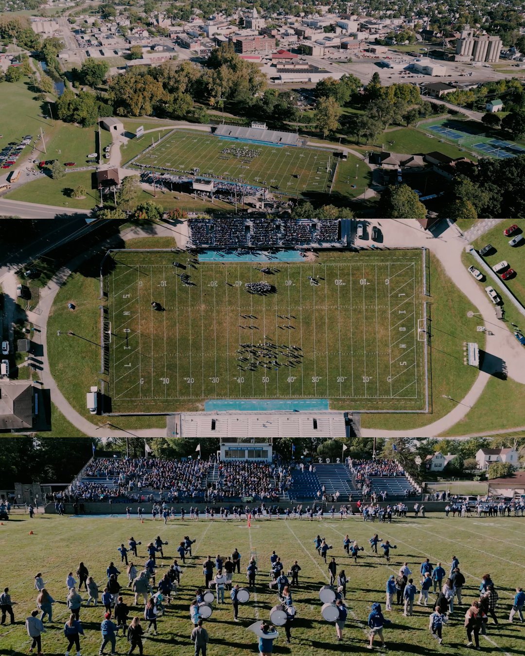 Aerial view of a football stadium with a marching band performing on the field, surrounded by a large crowd of spectators in the stands; city in the background.