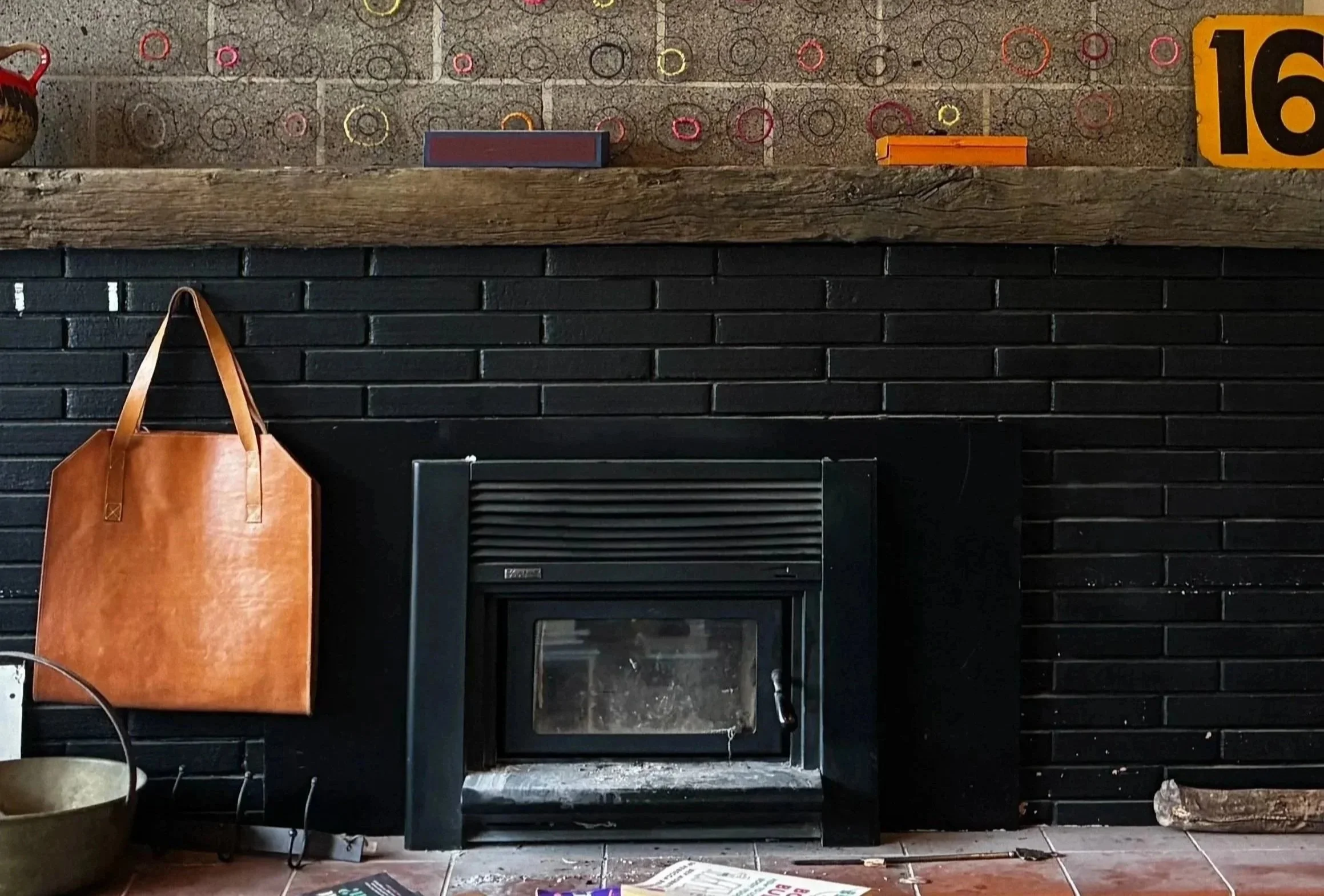 Gas fireplace in a living room with wall-mounted TV,  wooden shelves with decorative items, framed photographs, a potted plant, and a leather armchair near a large window.