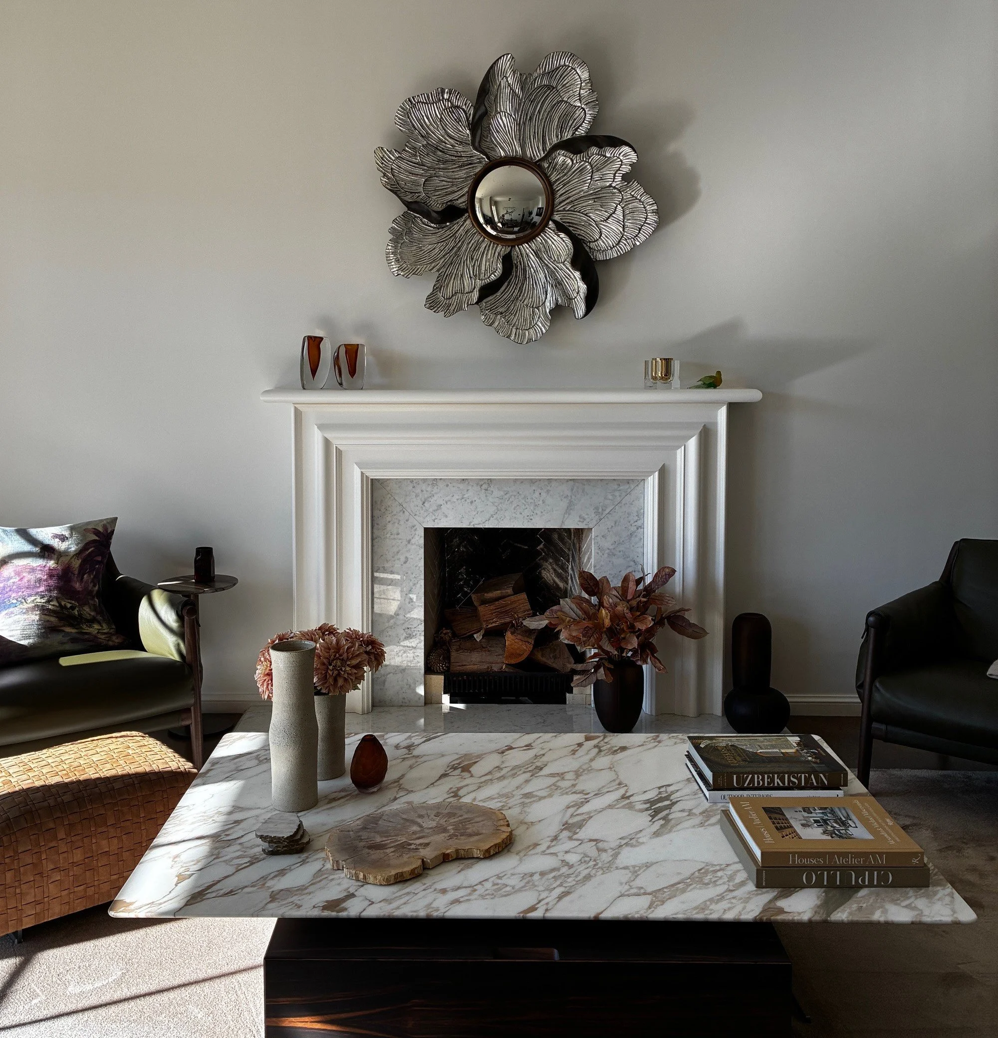 Gas fireplace in a living room with wall-mounted TV,  wooden shelves with decorative items, framed photographs, a potted plant, and a leather armchair near a large window.