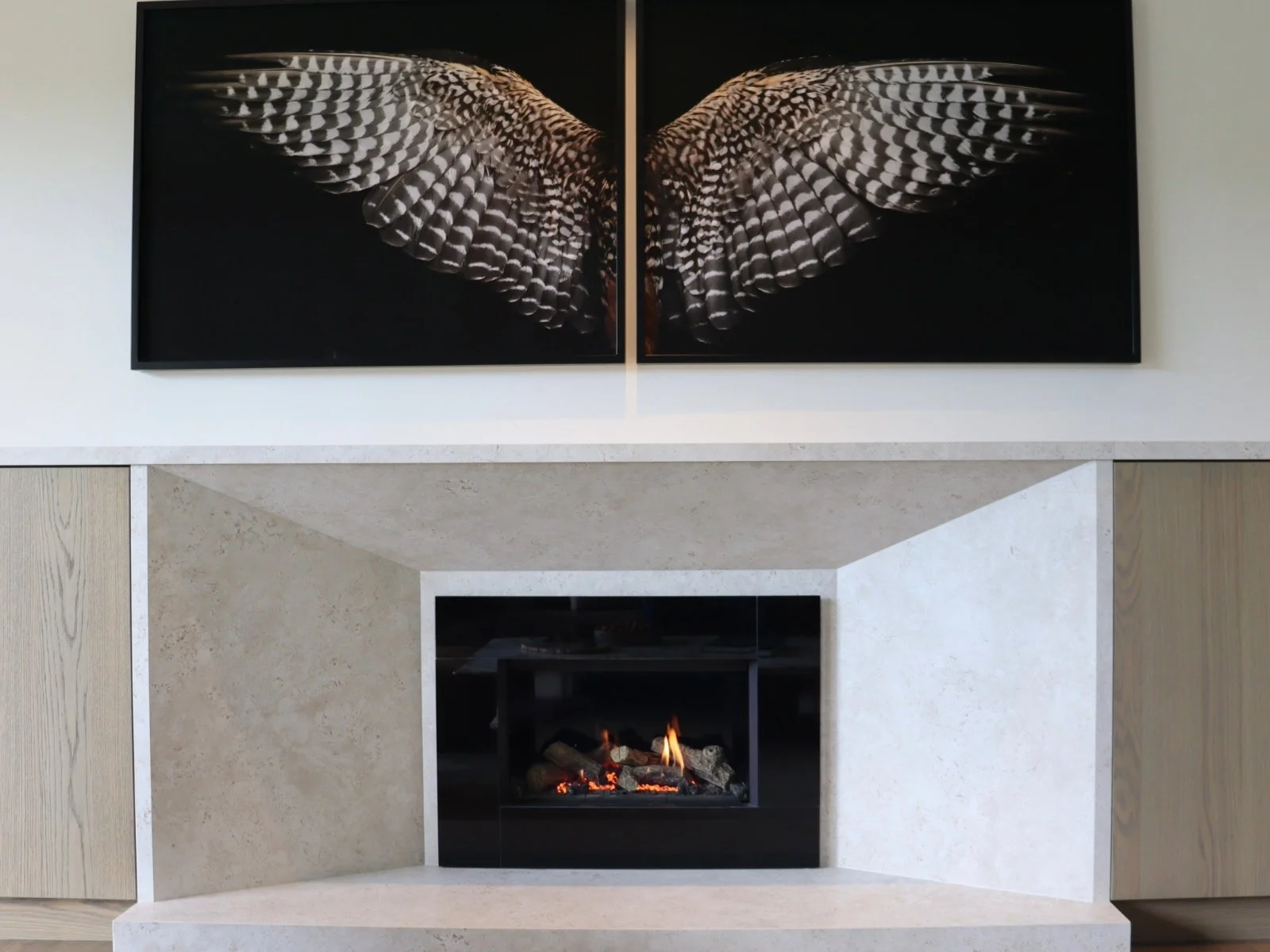 A living room fireplace with a modern design, surrounded by a light-colored stone mantel and two symmetrical wooden cabinets, with a fire burning inside.