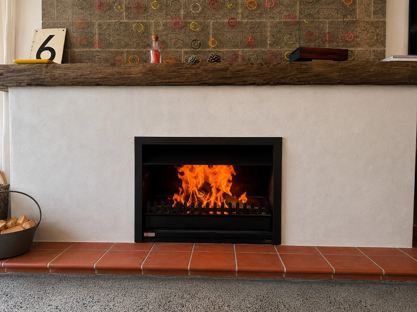 Stovax Studio 2 inbuilt wood fire with white brick surround and black steel mantel, a modern black lounge chair with an orange pillow, a side table with a potted plant, and a large window showing outdoor trees.