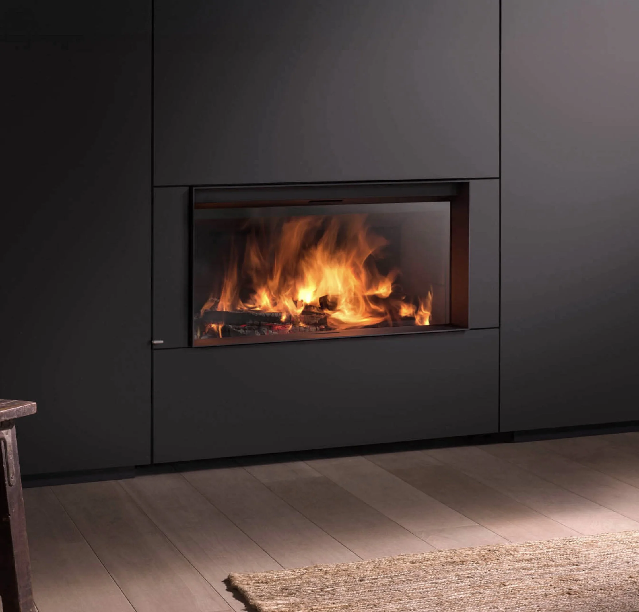 Modern black fireplace with visible flames, gray tiled wall, gray tiled floor, and a brown woven rug in front.
