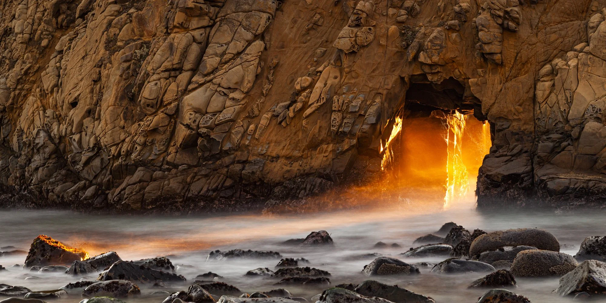 Sunset light through a keyhole arch at Pfeiffer Beach, Big Sur, California.