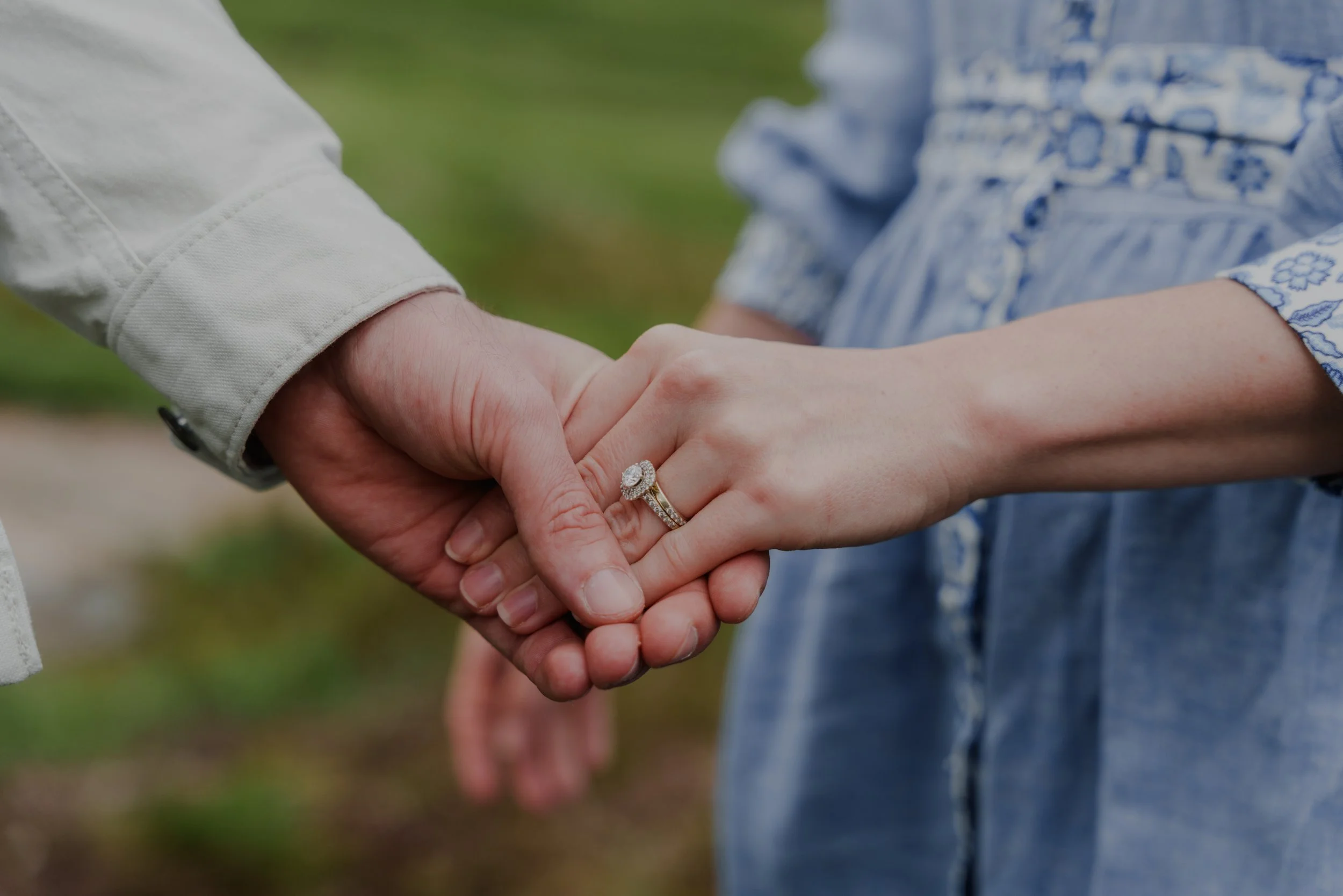 Close-up of a man and woman holding hands, showing the woman's engagement ring.