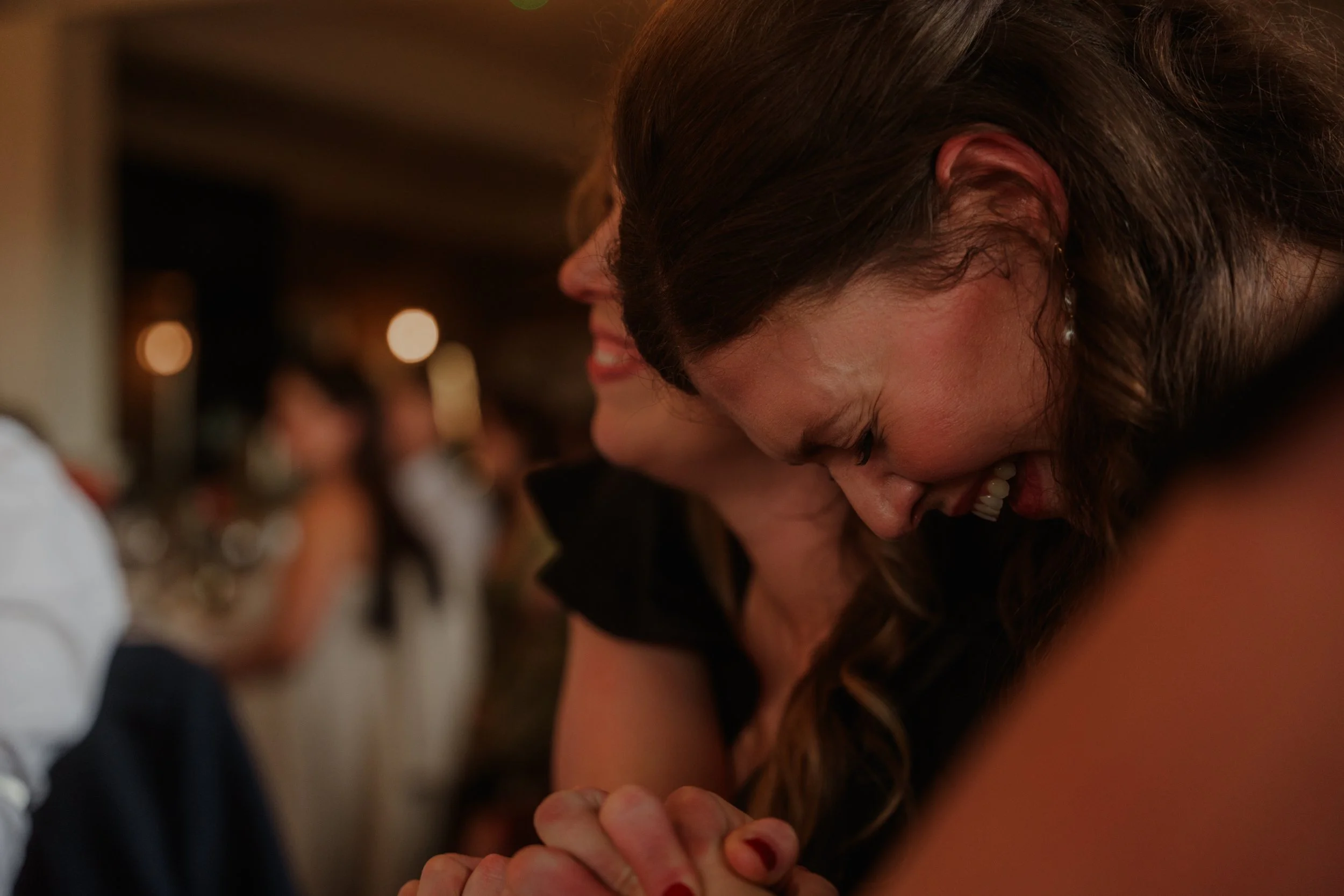 Two women with their eyes closed and hands clasped during a heartfelt moment at a social gathering.