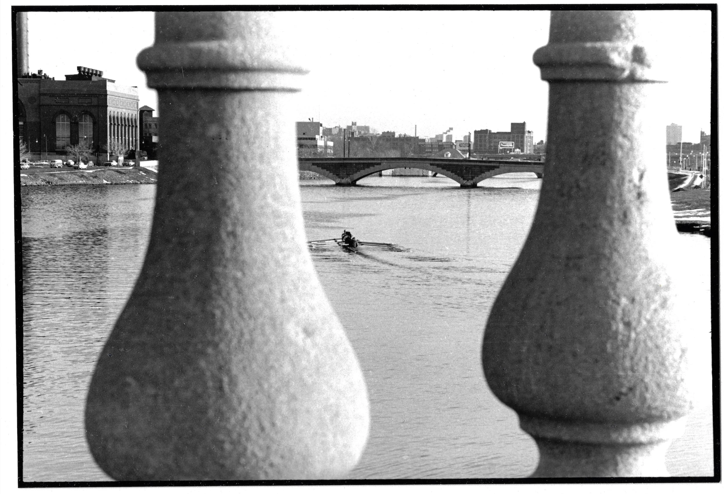 Scullers on the Charles glimpsed between the pillars of a bridge