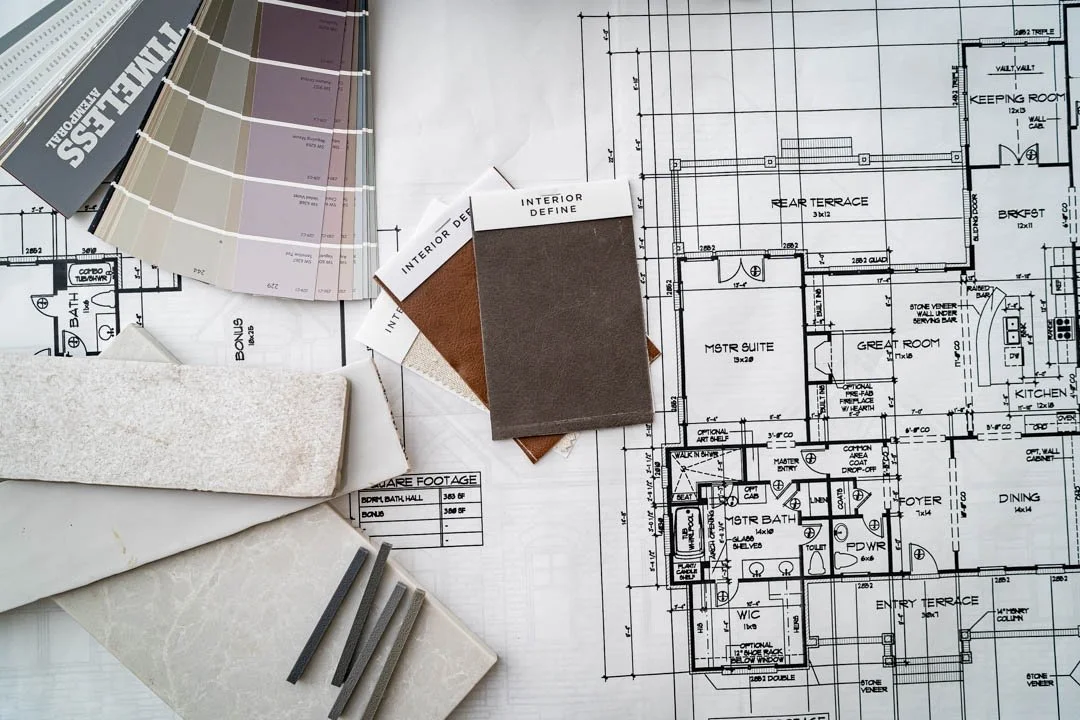 Flat lay photograph of blueprints, paint, and fabric samples used by an interior designer.