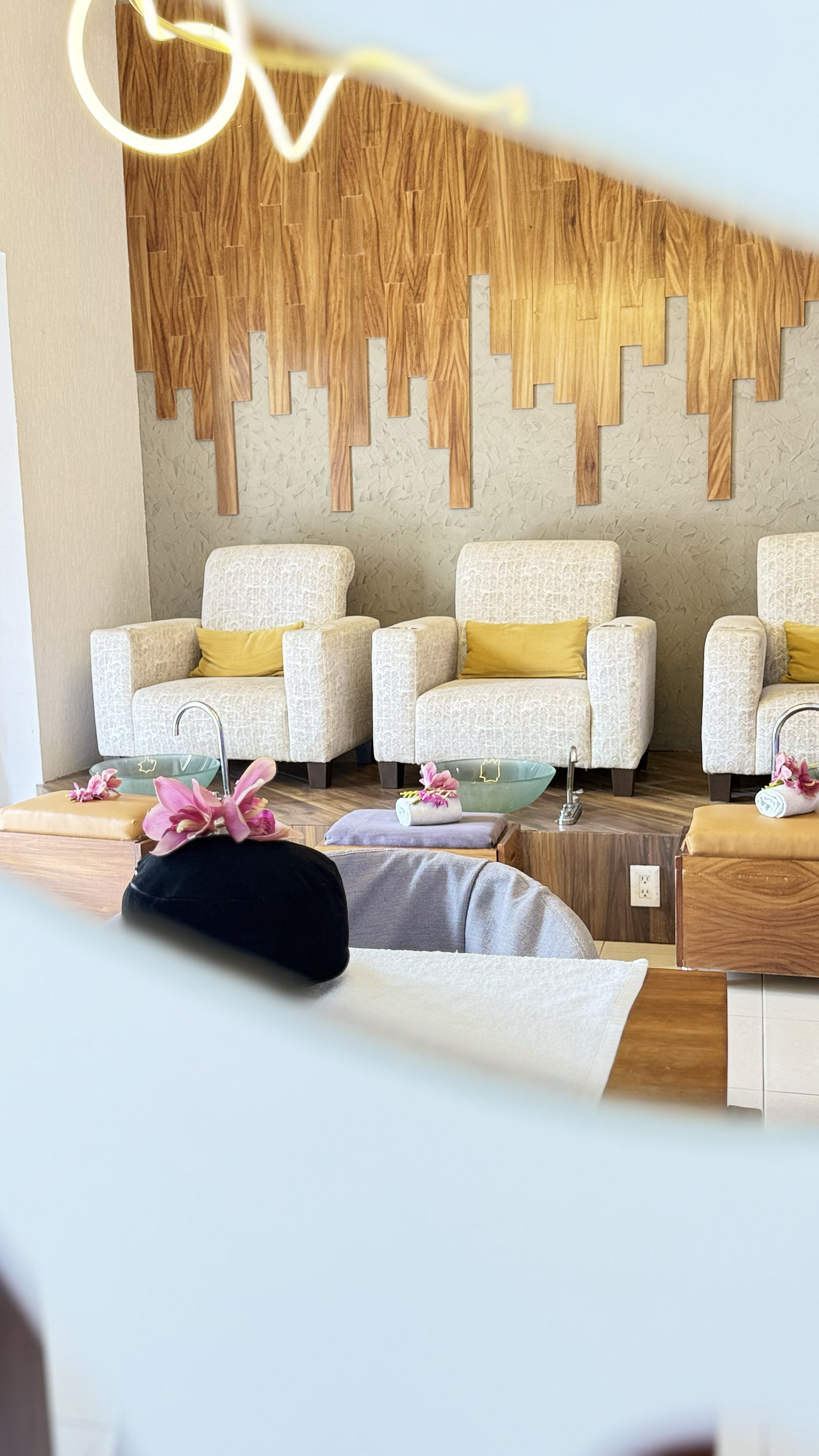 Sala de spa con sillones blancos, cojines amarillos, decoración de flores y artesanías de madera en la pared.