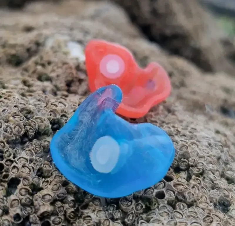 Close-up of a blue and a pink plastic or silicone turn signal lens on a rocky surface.