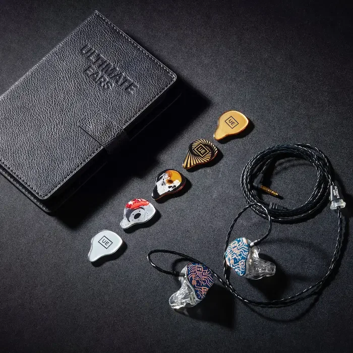 A black leather wallet with the brand name 'ULTIMATE EARS' embossed, several colorful custom in-ear monitors with different designs, a coiled black twisted cable with a 3.5mm jack, placed on a black surface.