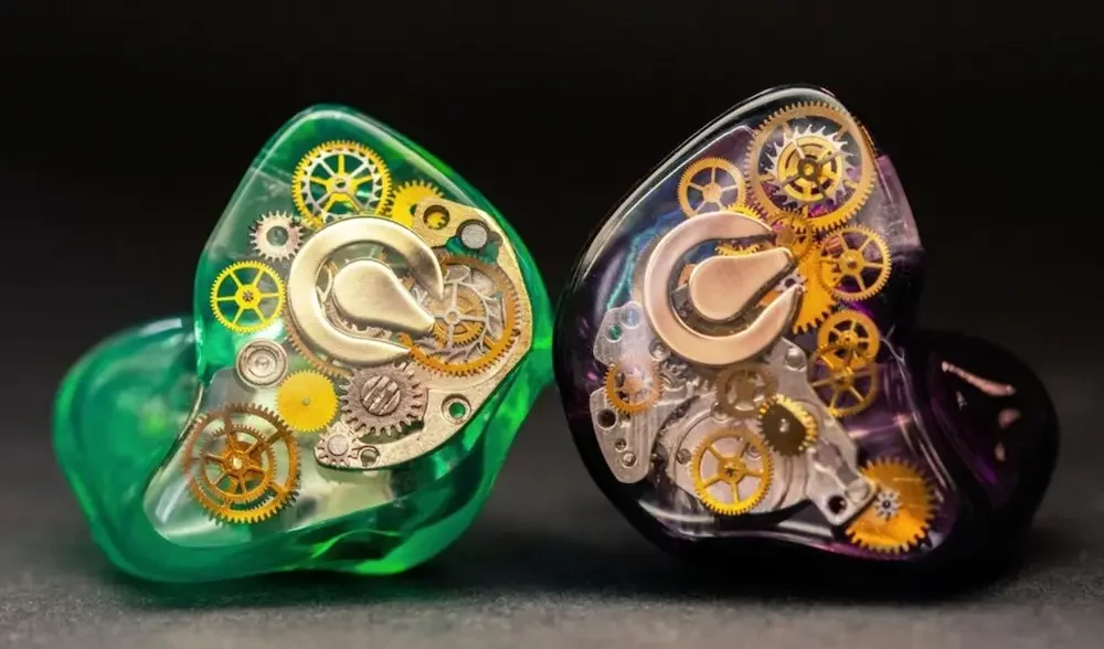 Close-up of two in-ear monitors with transparent cases, one green and one purple, showcasing internal gears and mechanisms.