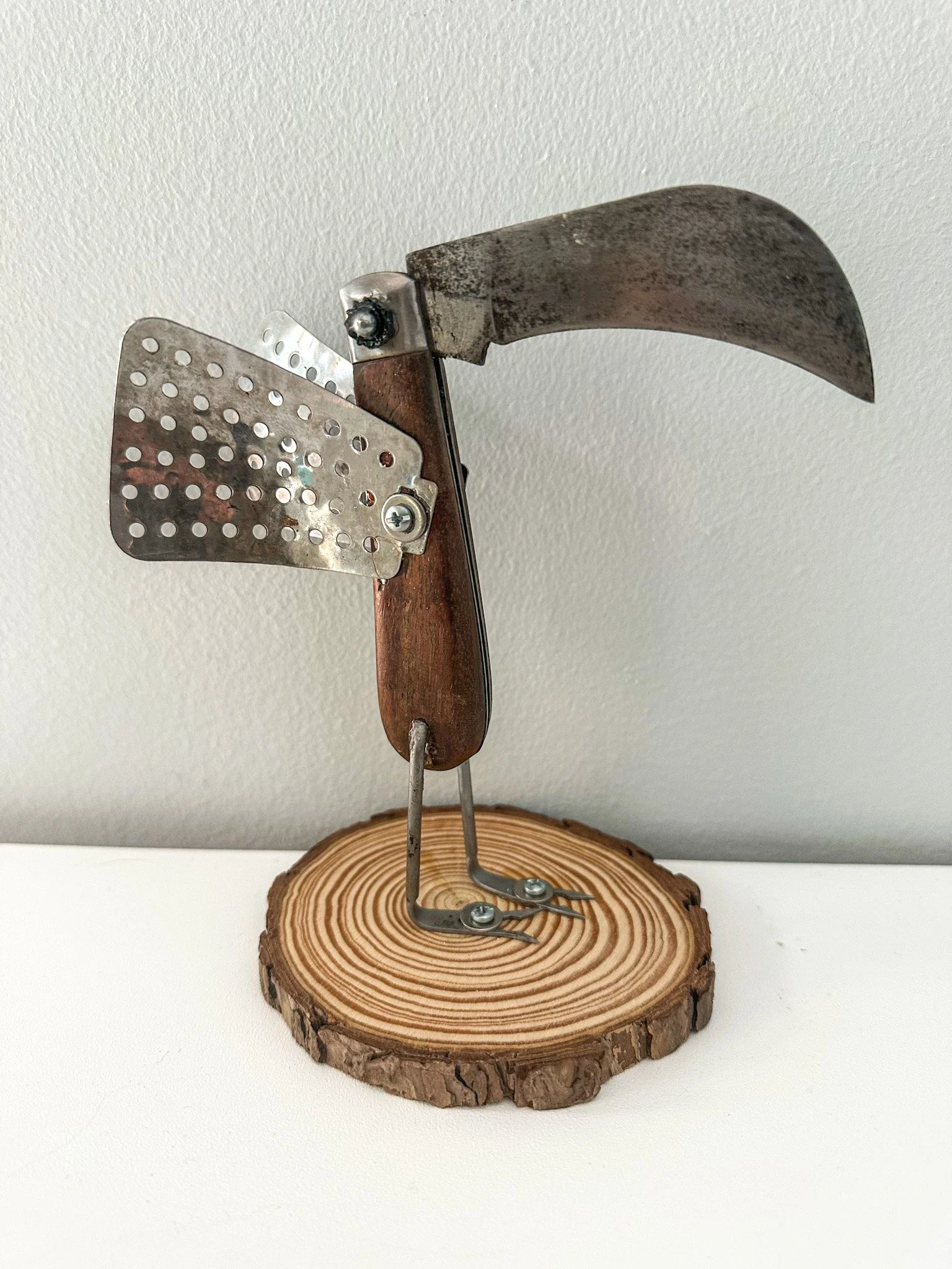 AVAILABLE: "Tina the Teenage Toucan".
6 X 6 X 4
Constructed of a vintage Japanese pocket knife, pickle forks, vegetable steamer leaves, K-lock nuts, ball bearings, wooden disc from tree branch.