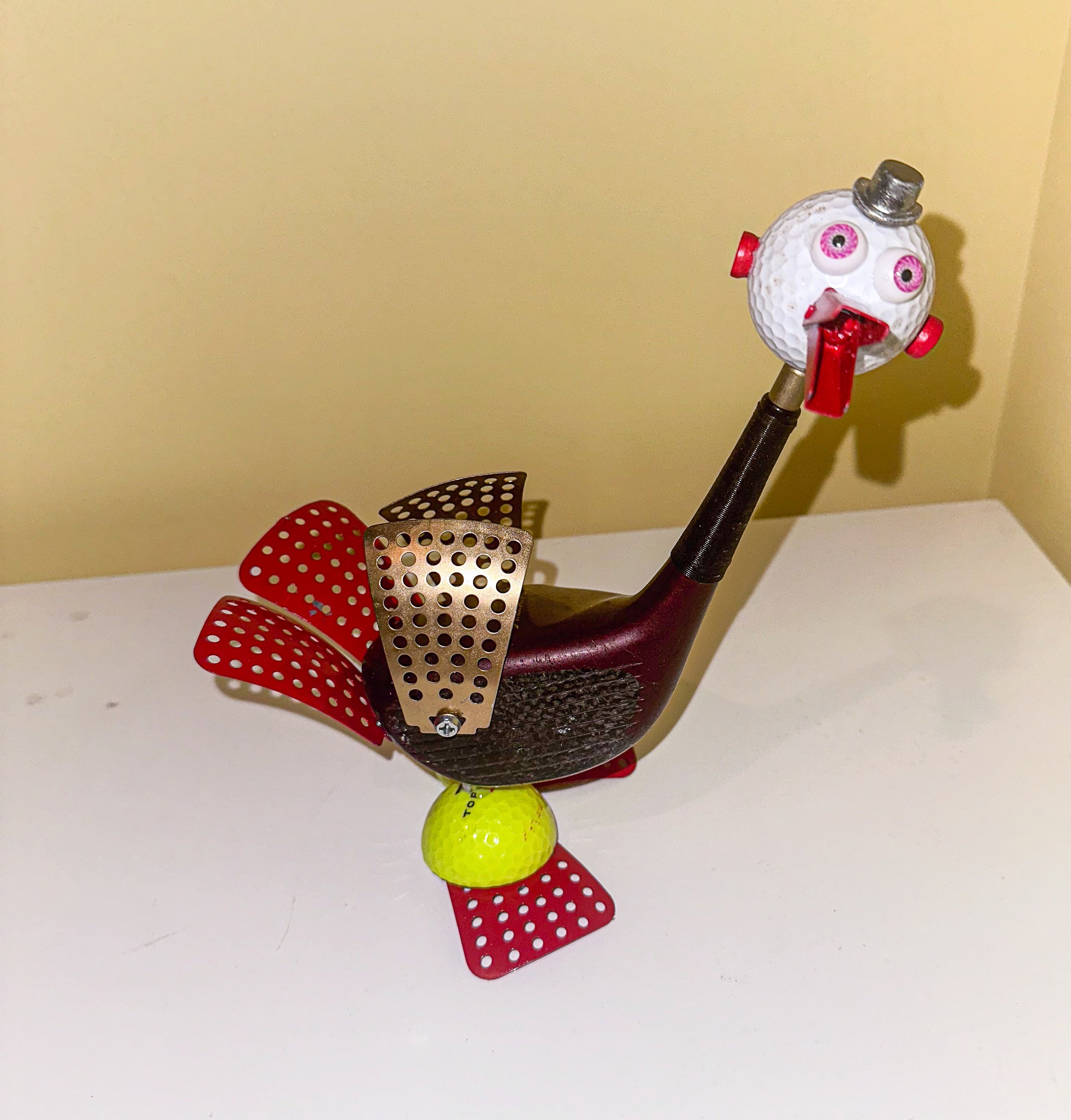 SOLD, "Bertha Birdie".
“Bertha Birdie” aka “The Golfer’s Talisman”
Old driver, golf balls, golf tees, vegetable steamer leaves, toggle bolt, doll eyes, monopoly piece.
Bertha Birdie is the daughter of Bubba Birdie (named after his favorite driver