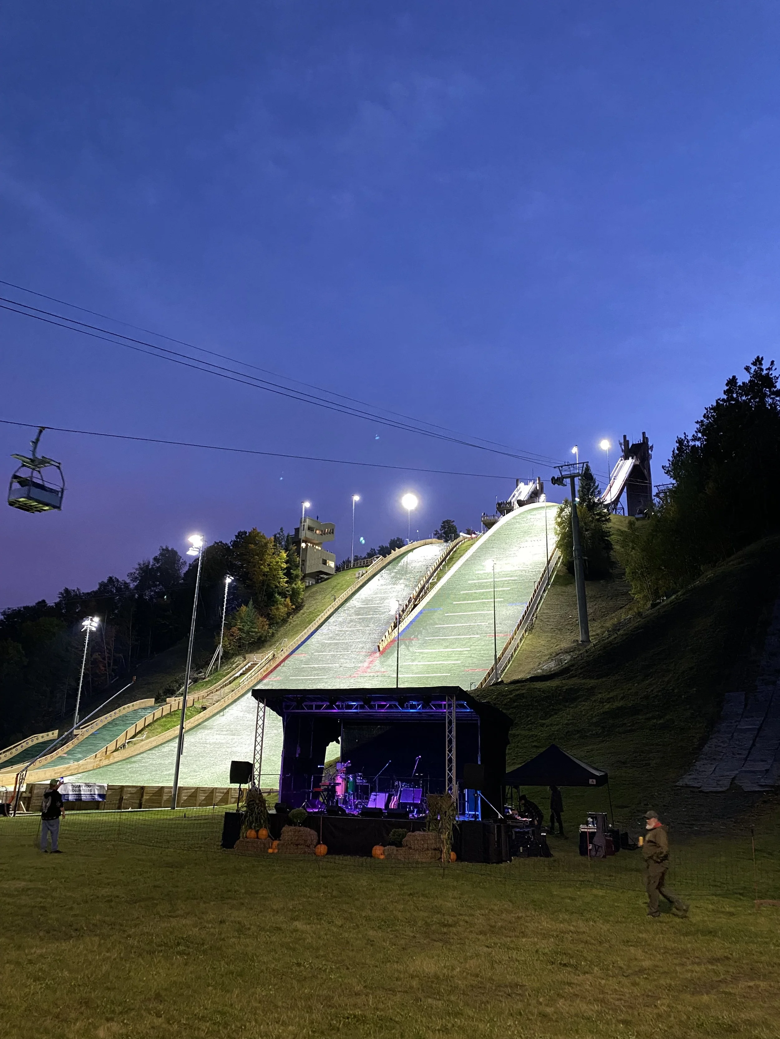 Ski jumps at night with lights on them and a band playing in front.