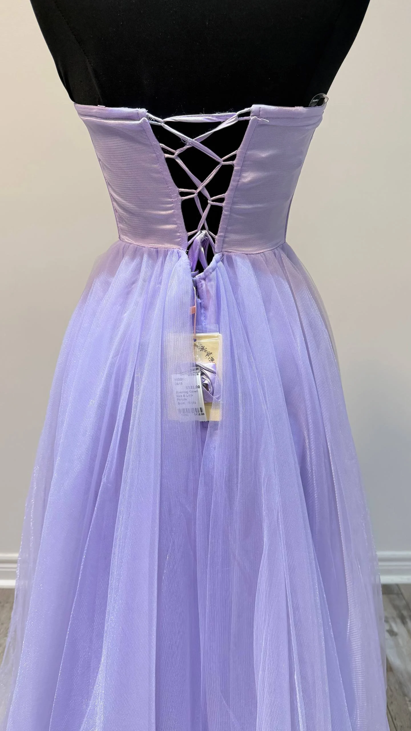 A lavender-colored dress on a display mannequin, featuring a lace-up back with ribbon details and a flowing tulle skirt.