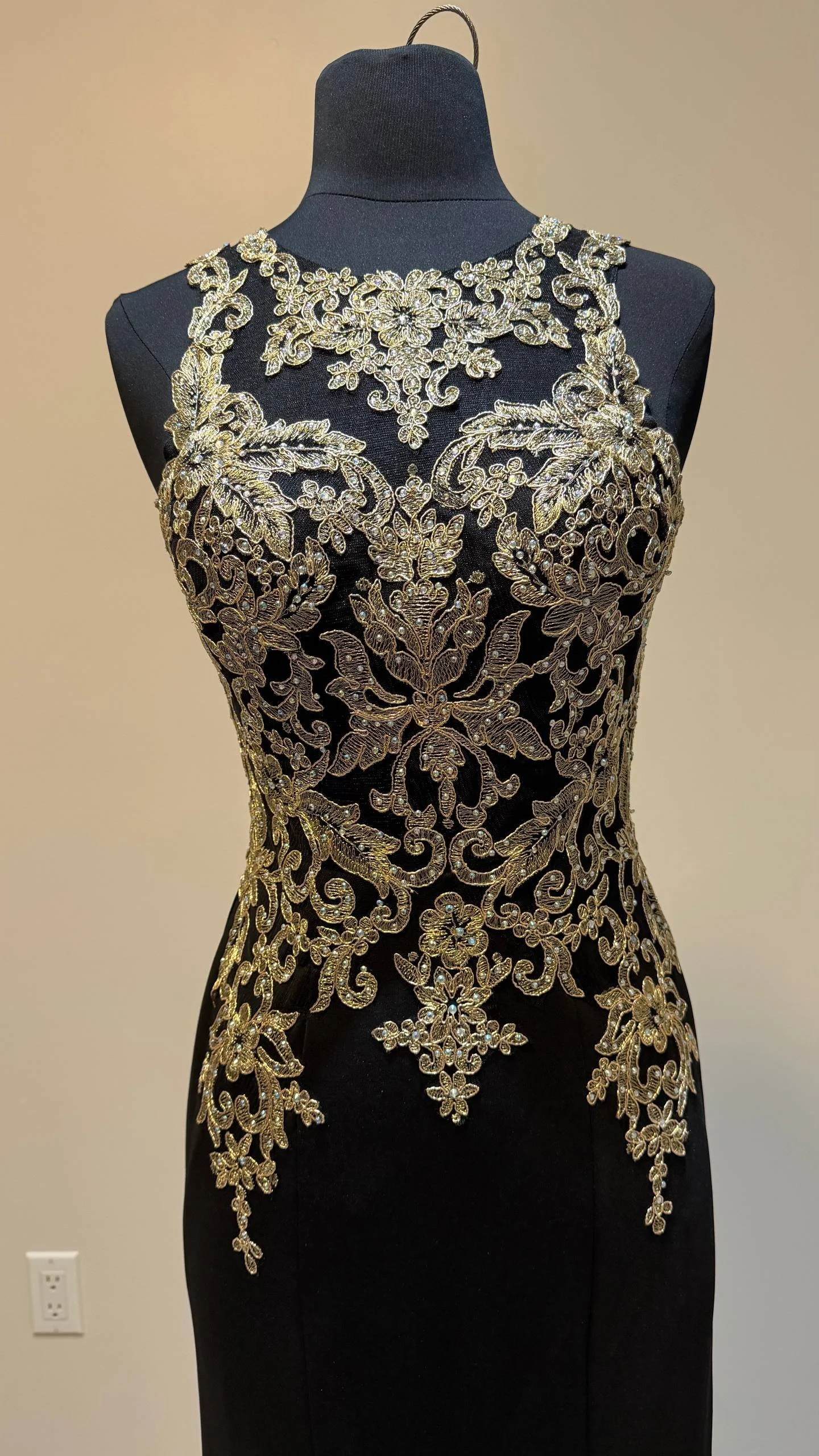 A black evening gown with intricate gold embroidery and embellishments displayed on a mannequin.