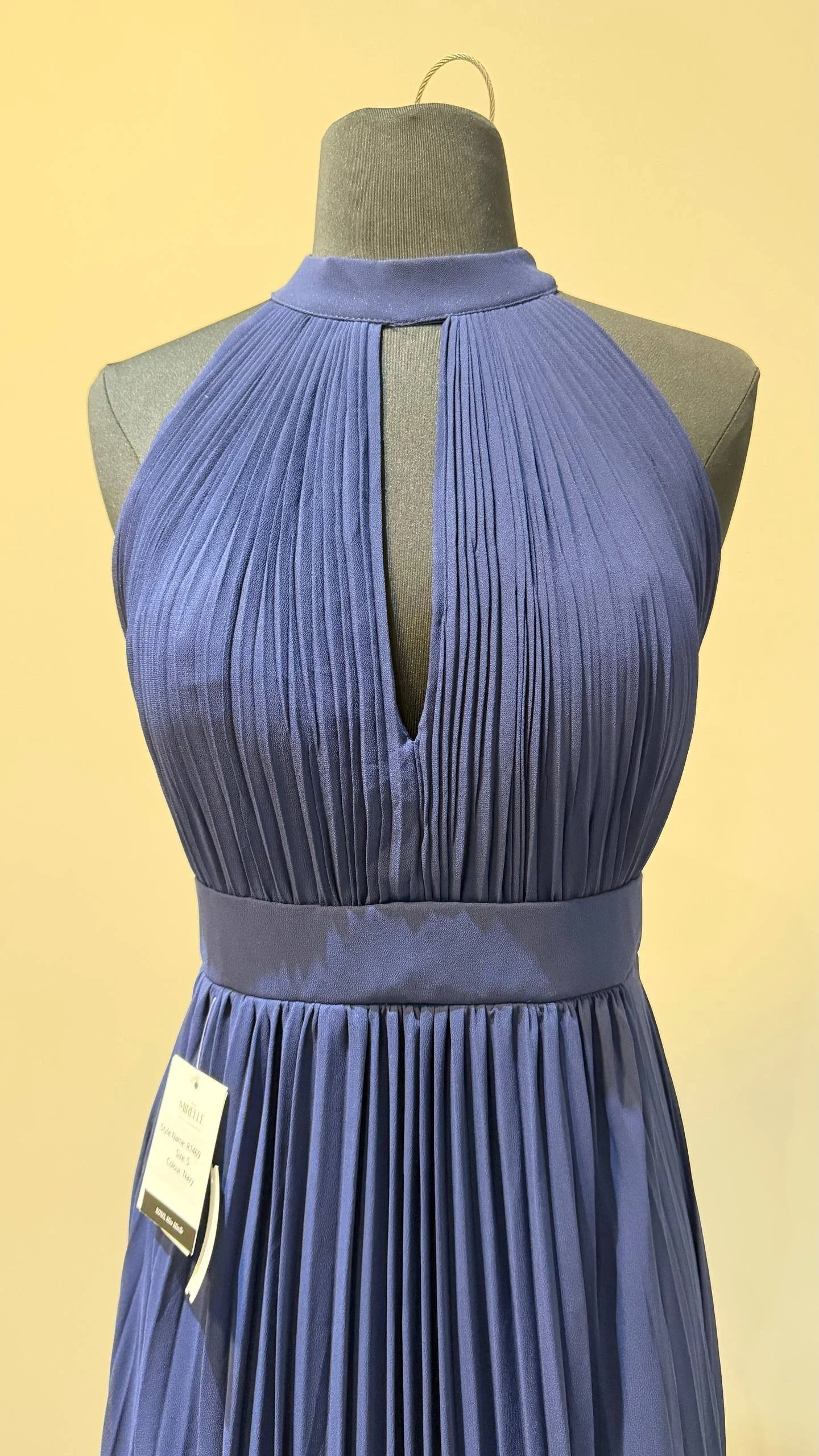 A navy blue pleated dress on a mannequin with a halter neckline and a keyhole cutout at the chest.