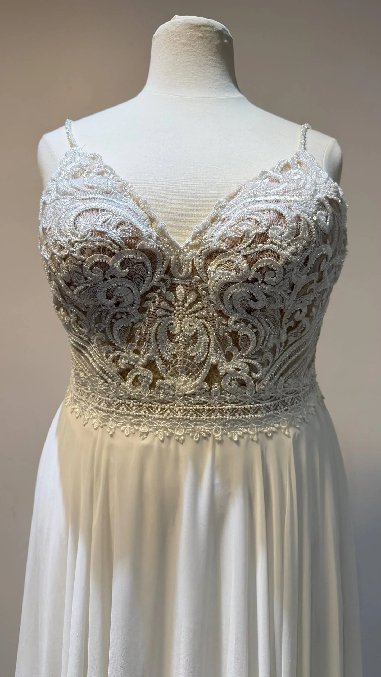 A wedding dress with intricate lace and beadwork on the bodice, featuring spaghetti straps and a flowing satin skirt.