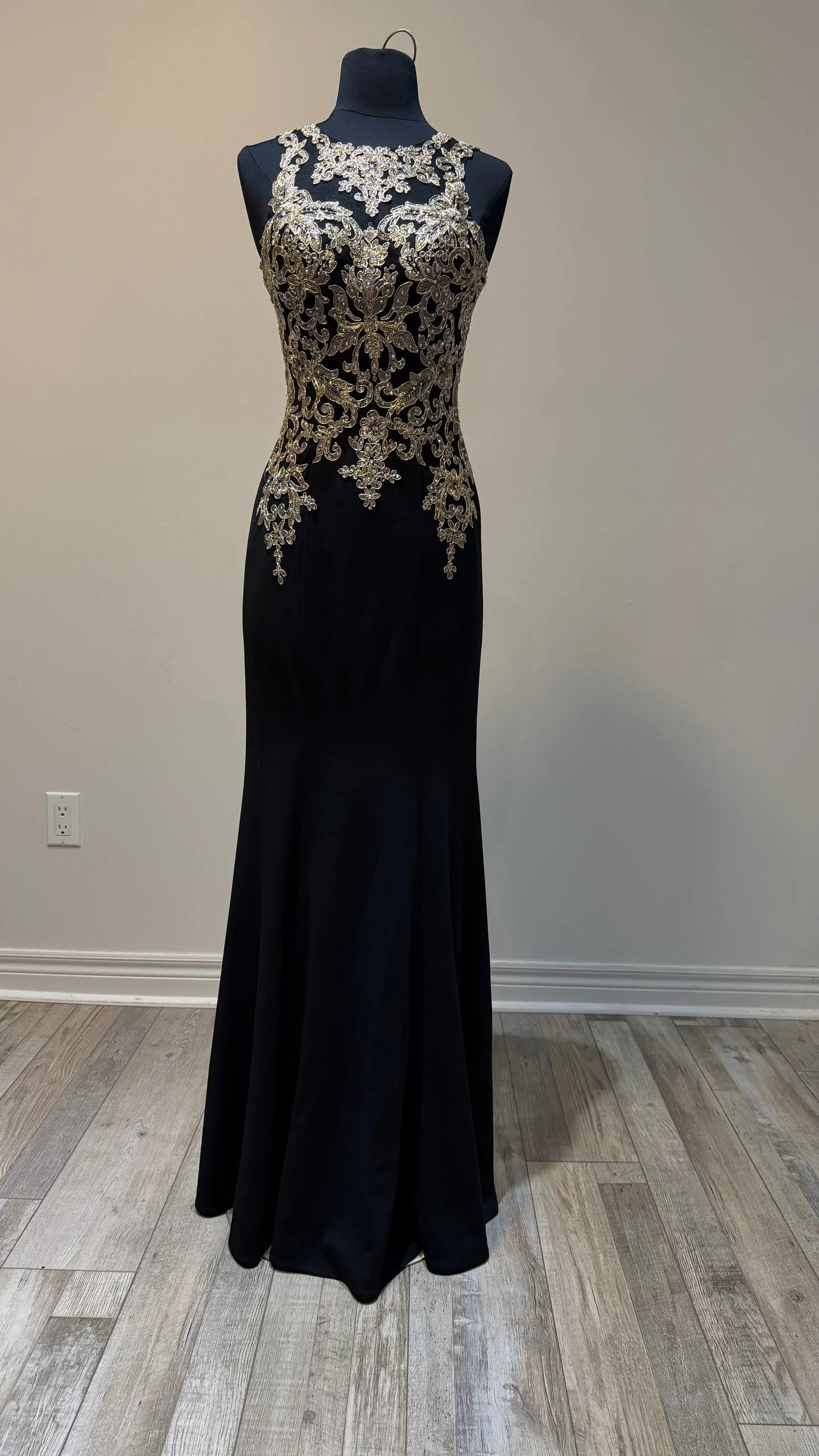 Black evening gown on a display mannequin with silver and gold embroidery on the bodice and upper part of the skirt, sleeveless with a high neckline.