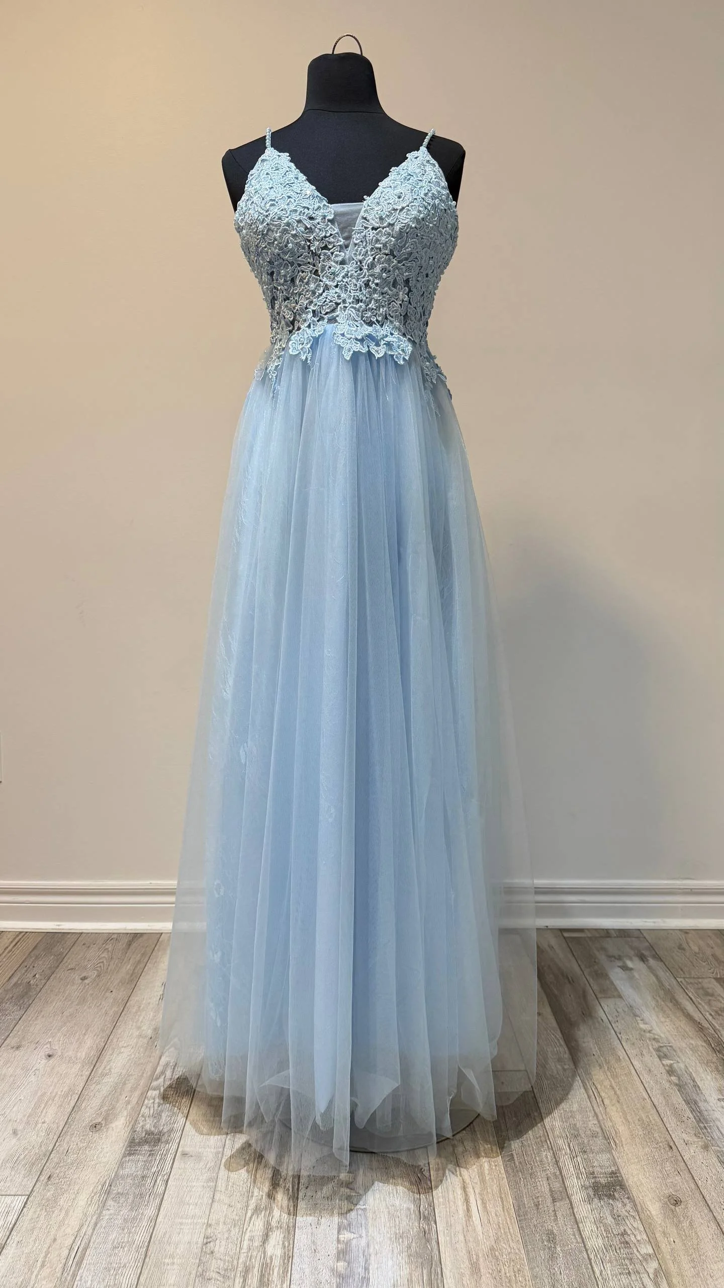 A light blue evening gown with lace bodice and chiffon skirt on a dress form against a plain wall.