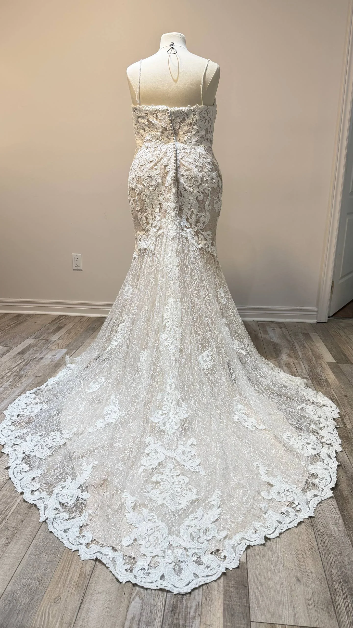 Elegant white lace wedding dress displayed on a mannequin, featuring a fitted bodice, spaghetti straps, intricate lace detailing, and a long train with scalloped lace edges.