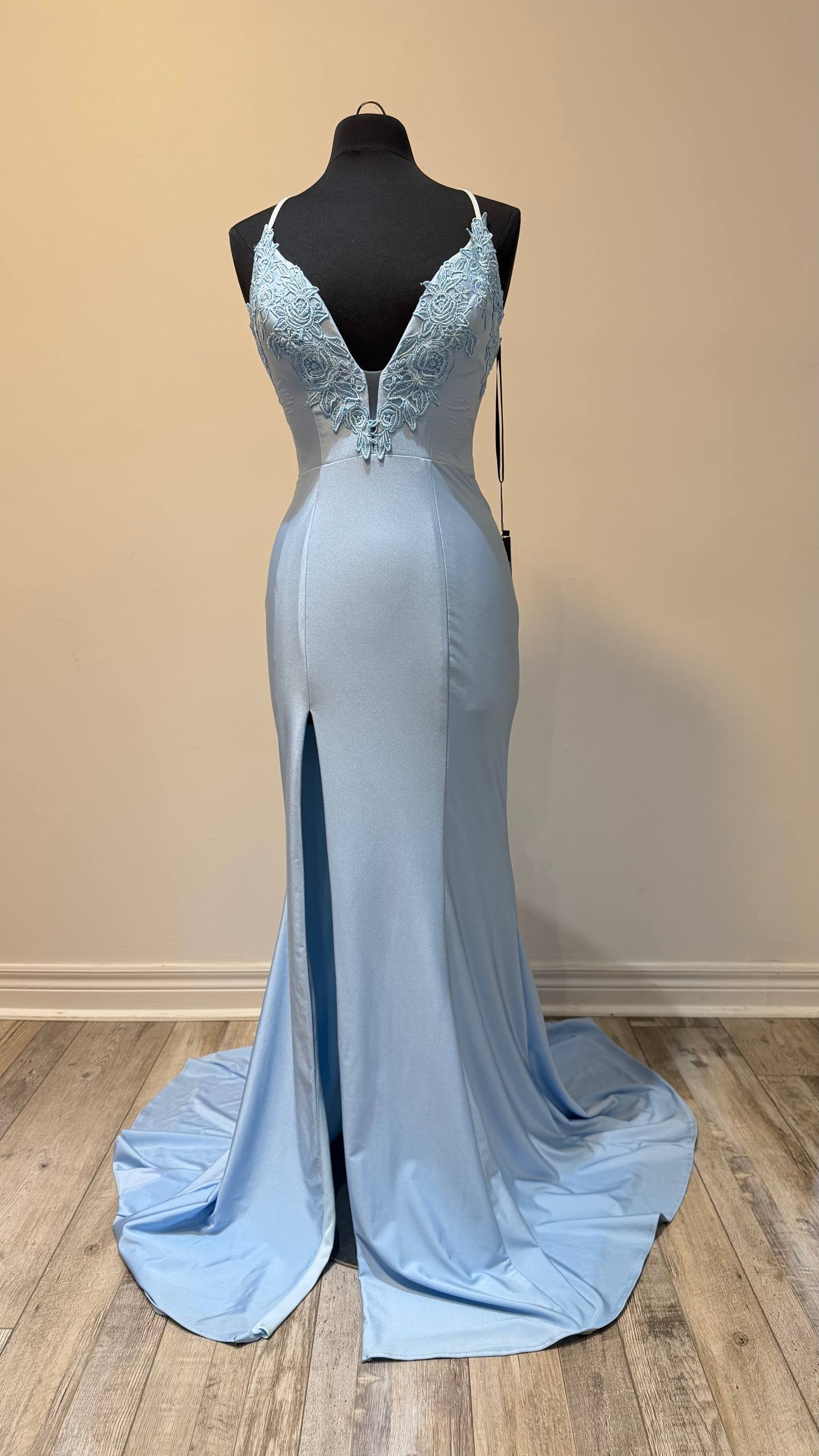 A light blue satin wedding dress on a mannequin, featuring a deep V-neckline with floral lace embroidery and a front slit, with a long train flowing on the wooden floor.